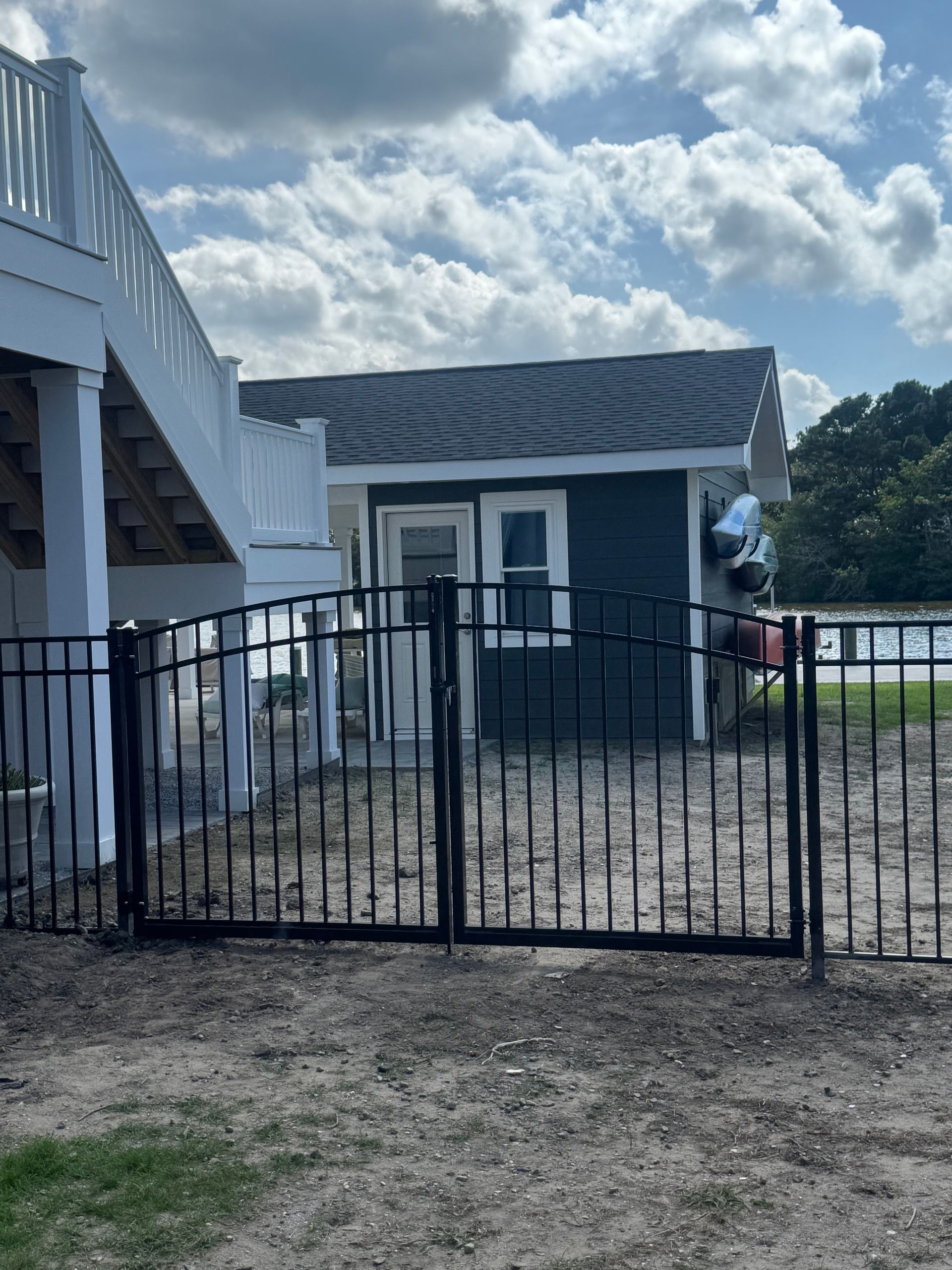 Black metal gate in front of a blue shed with a white deck on the left side under a cloudy sky.