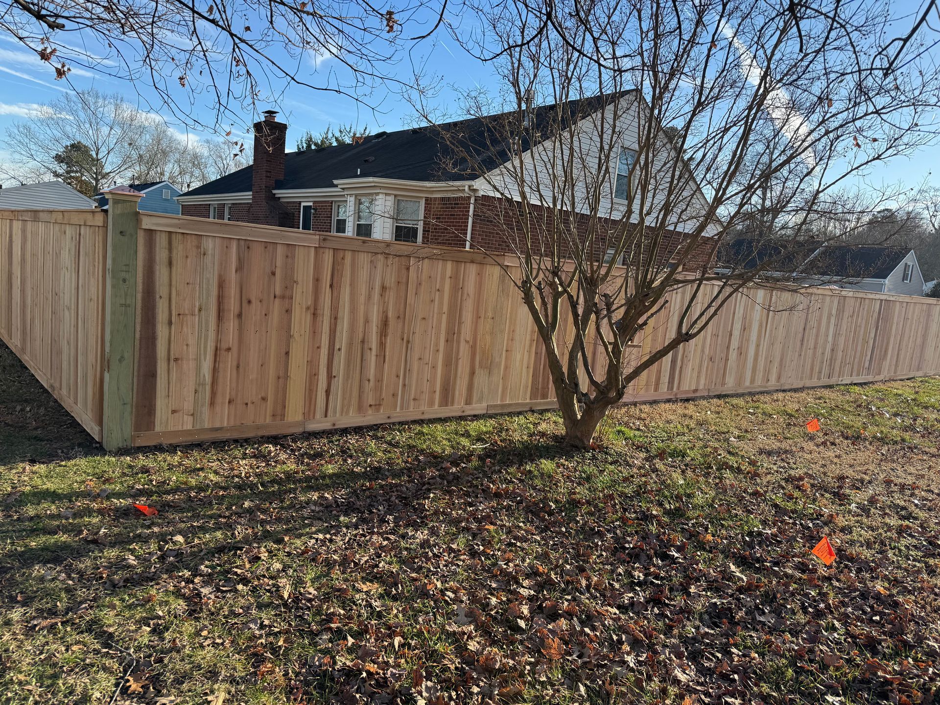 Wooden fence in a yard with a house in the background and a leafless tree in the foreground.