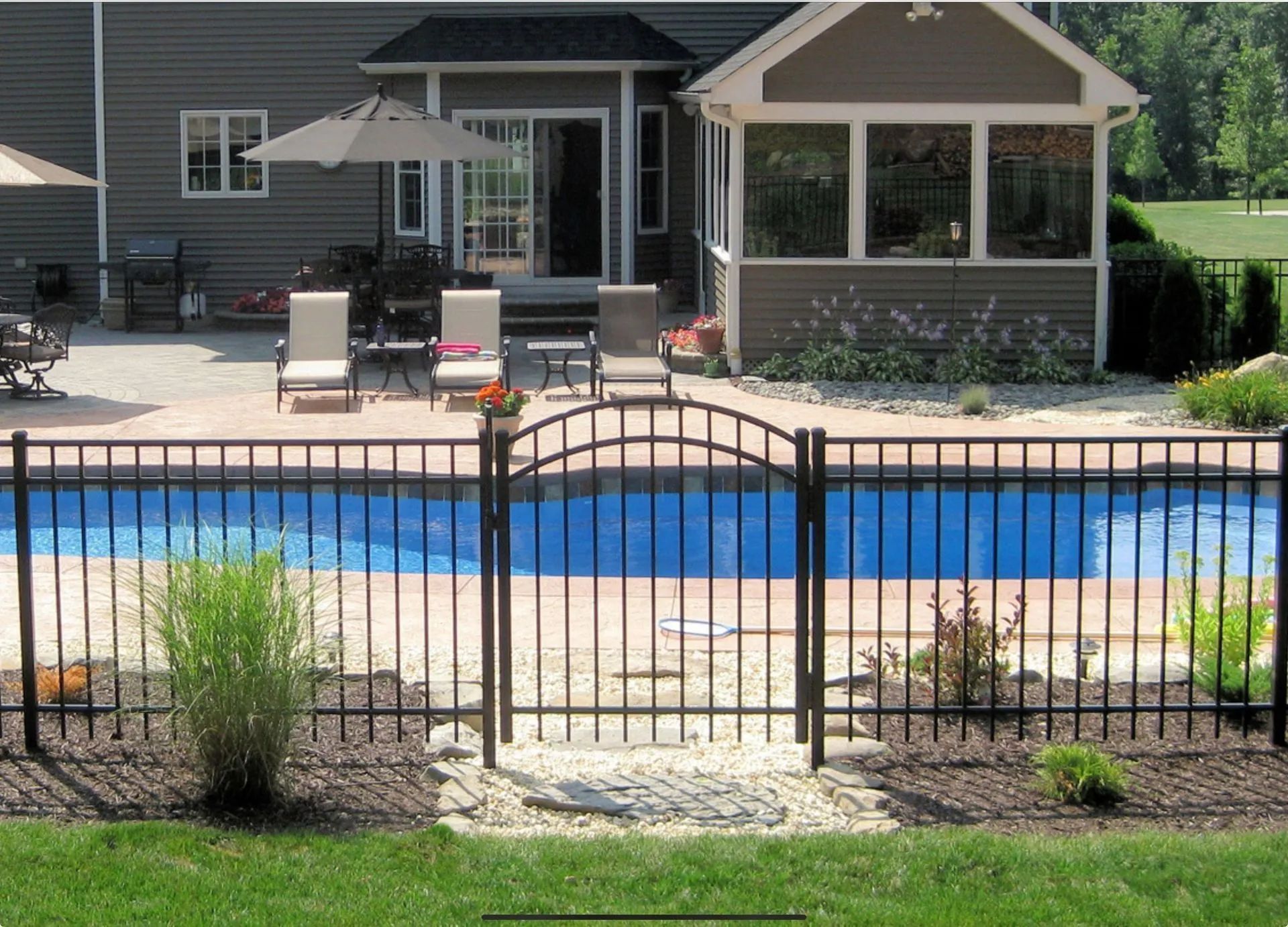 Black wrought iron fence around a swimming pool with a gate, house in the background.
