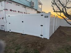 White vinyl fence surrounding a light blue house, with a sunset in the background.