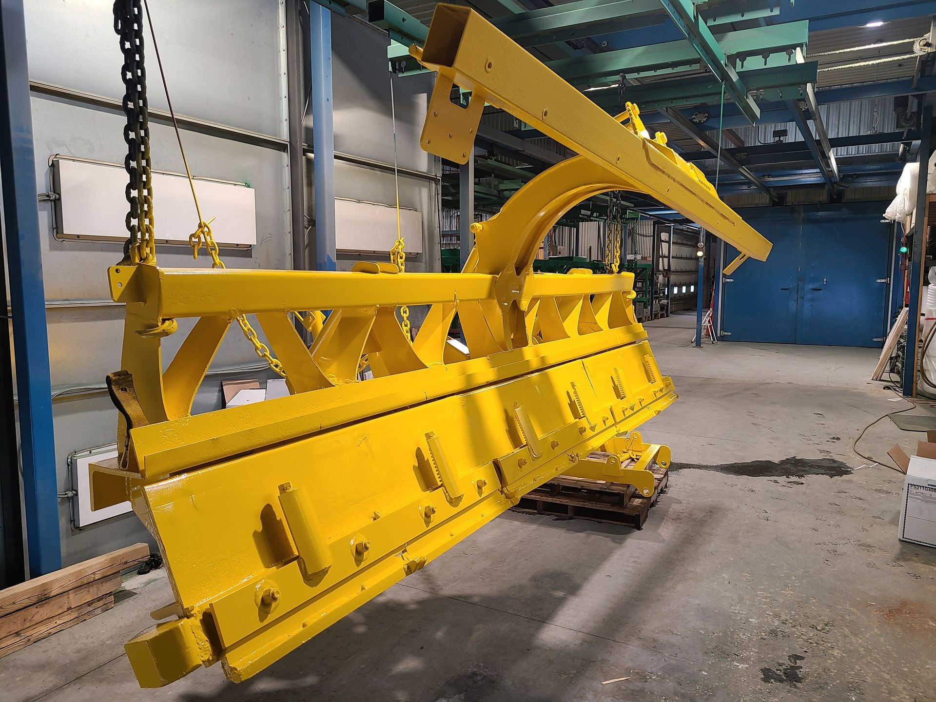Un gros morceau de métal jaune est suspendu à des chaînes dans un entrepôt.