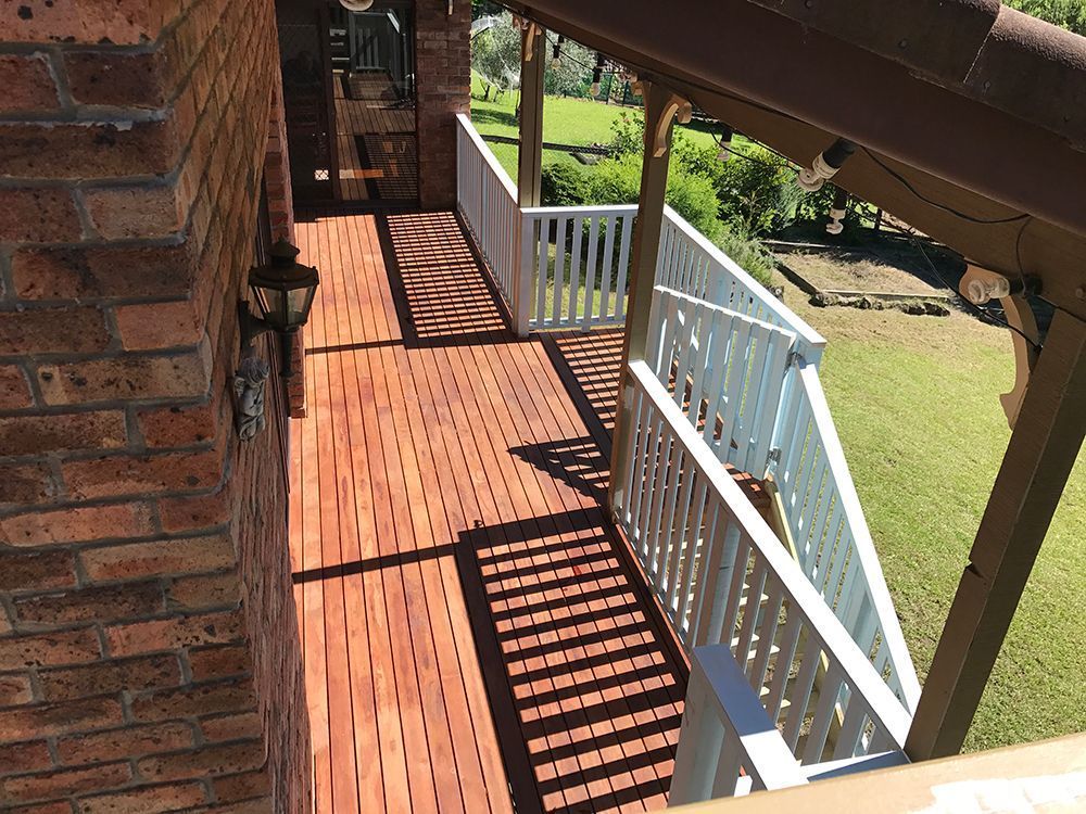 A Wooden Deck with A White Railing and A Brick Wall — Tradewind Building Maintenance in Woonona,NSW