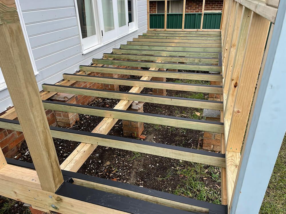 A Wooden Deck Is Being Built on The Side of A House — Tradewind Building Maintenance in Balgownie,NSW