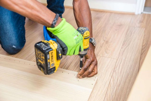 A carpenter uses as in impact driver to fasten flooring panels to the sub floor with screws