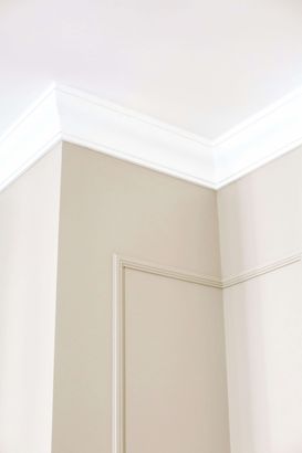 Installation of crown moulding in the corner of a room with white walls and a white ceiling.