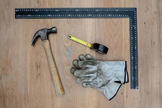 A hammer , measuring tape , and gloves are on a wooden table.