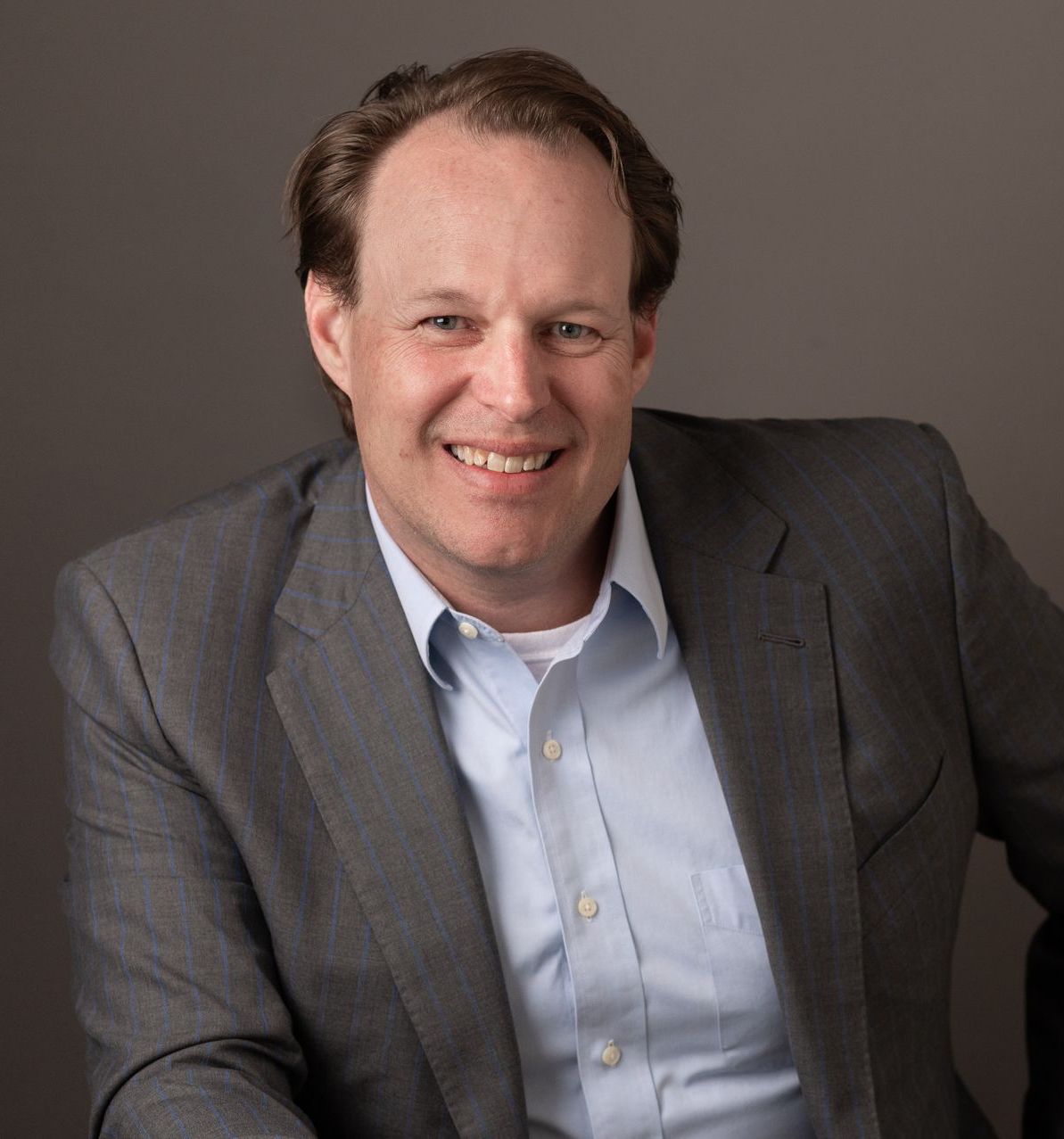 A man in a suit and blue shirt is smiling for the camera