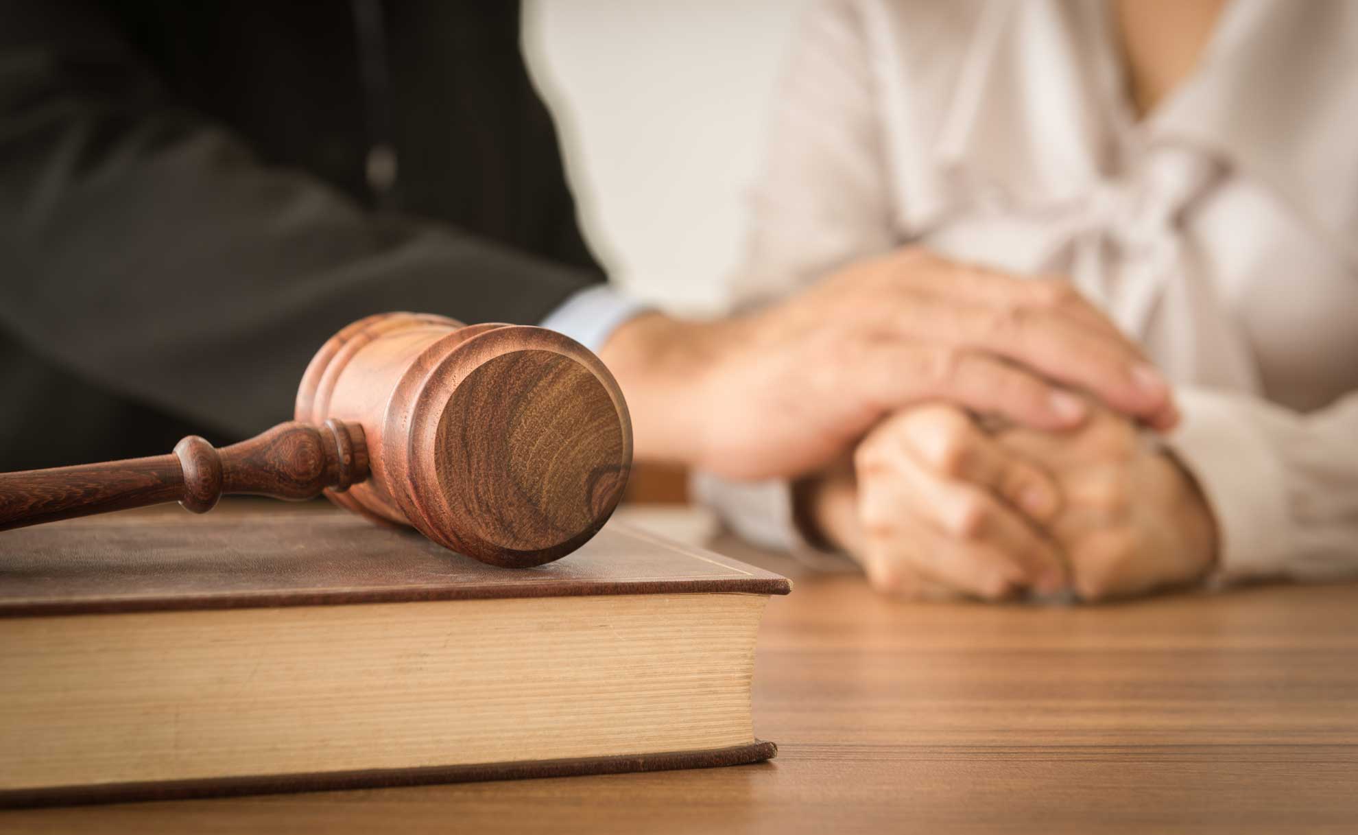 Marteau sur un livre juridique, main d'une personne sur celle d'une autre. Soutien émotionnel, possibilité de cadre juridique.