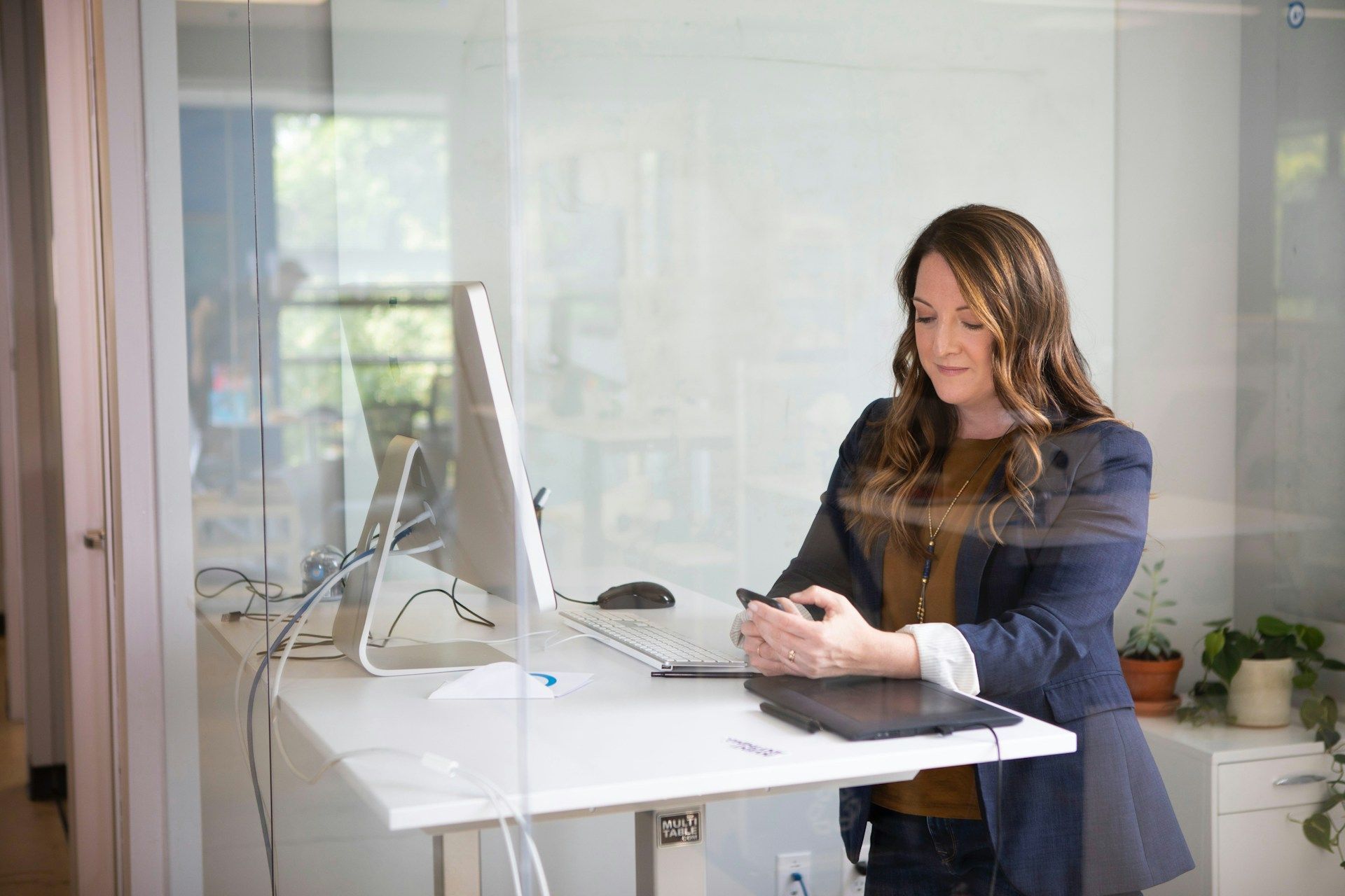 A woman is standing at a standing desk looking at her phone.