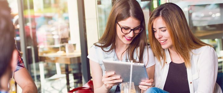 Two women are sitting at a table looking at a tablet.