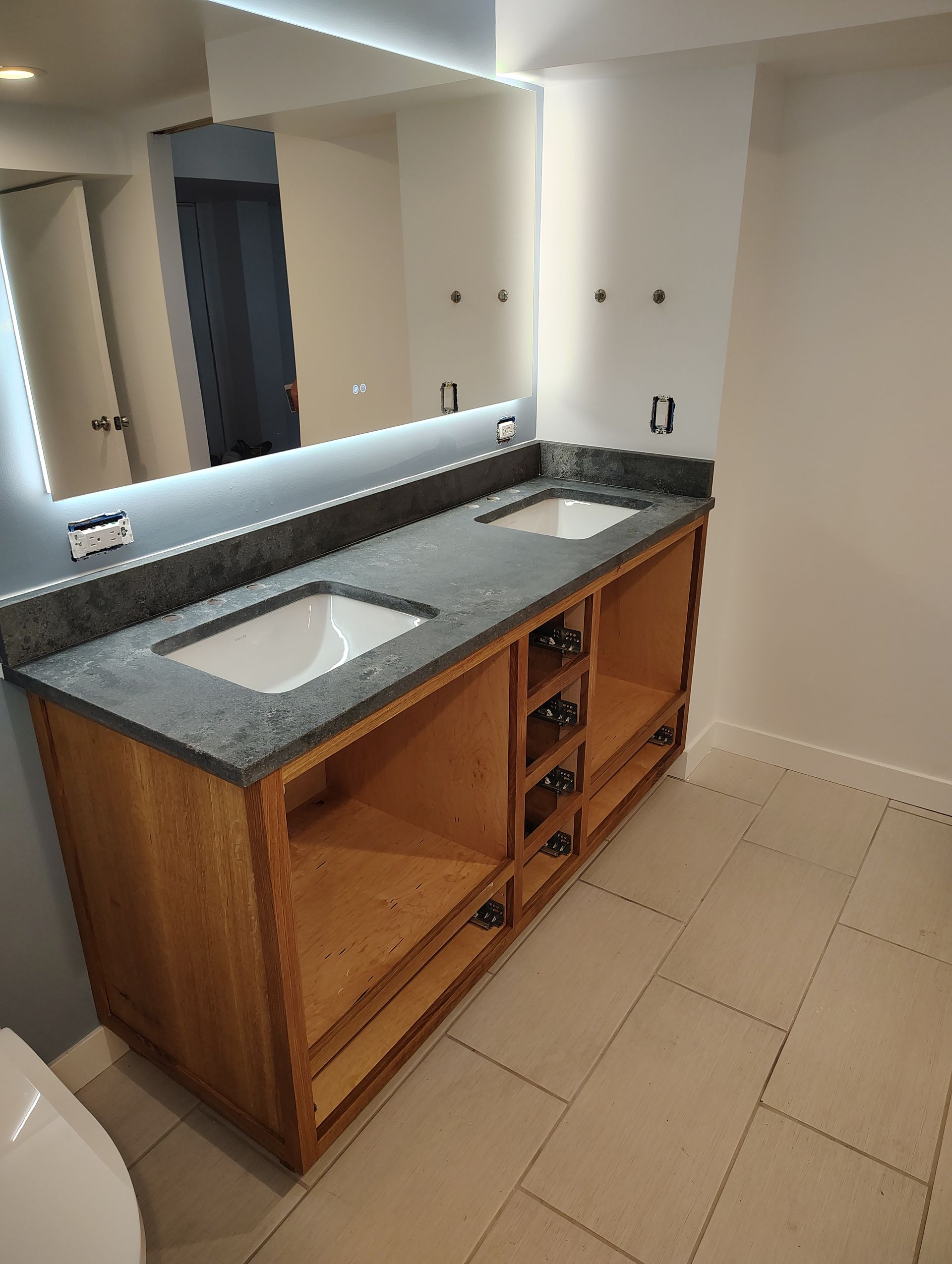 Bathroom vanity with granite countertop, two sinks, and wood cabinets. Mirror above.