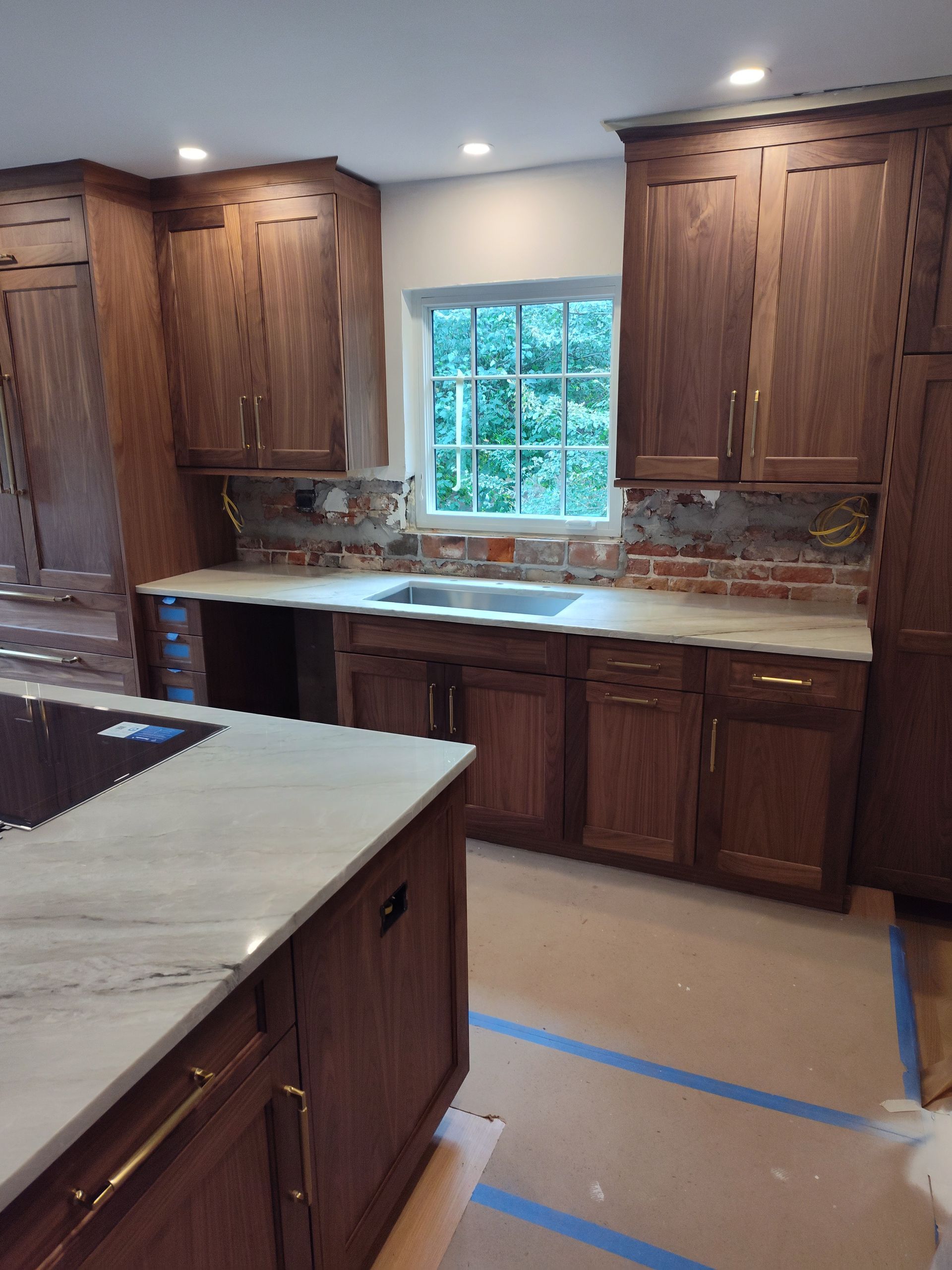 Kitchen with dark wood cabinets, white countertops, and brick backsplash.