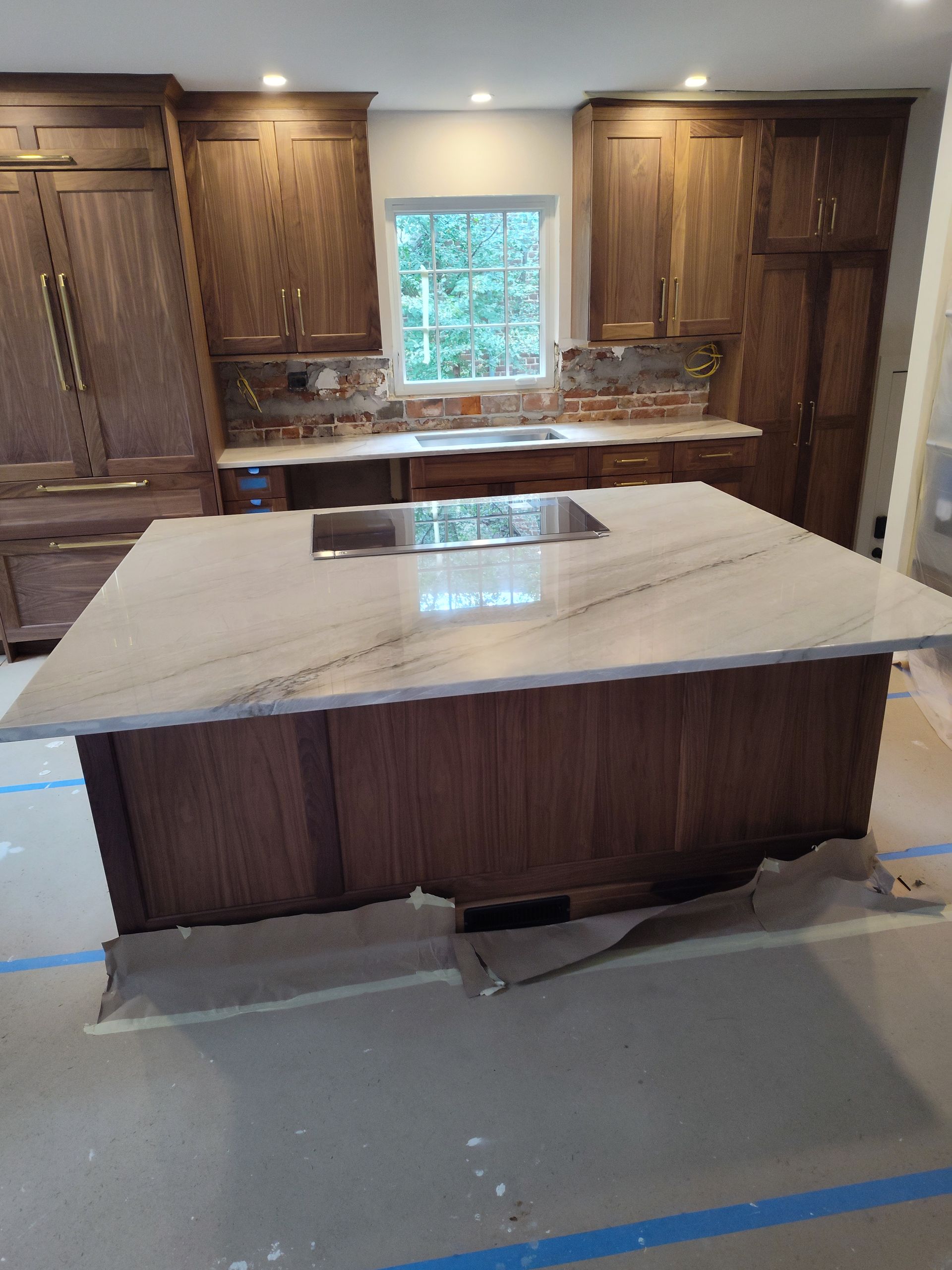 Kitchen with wood cabinets, marble island, and a cooktop.