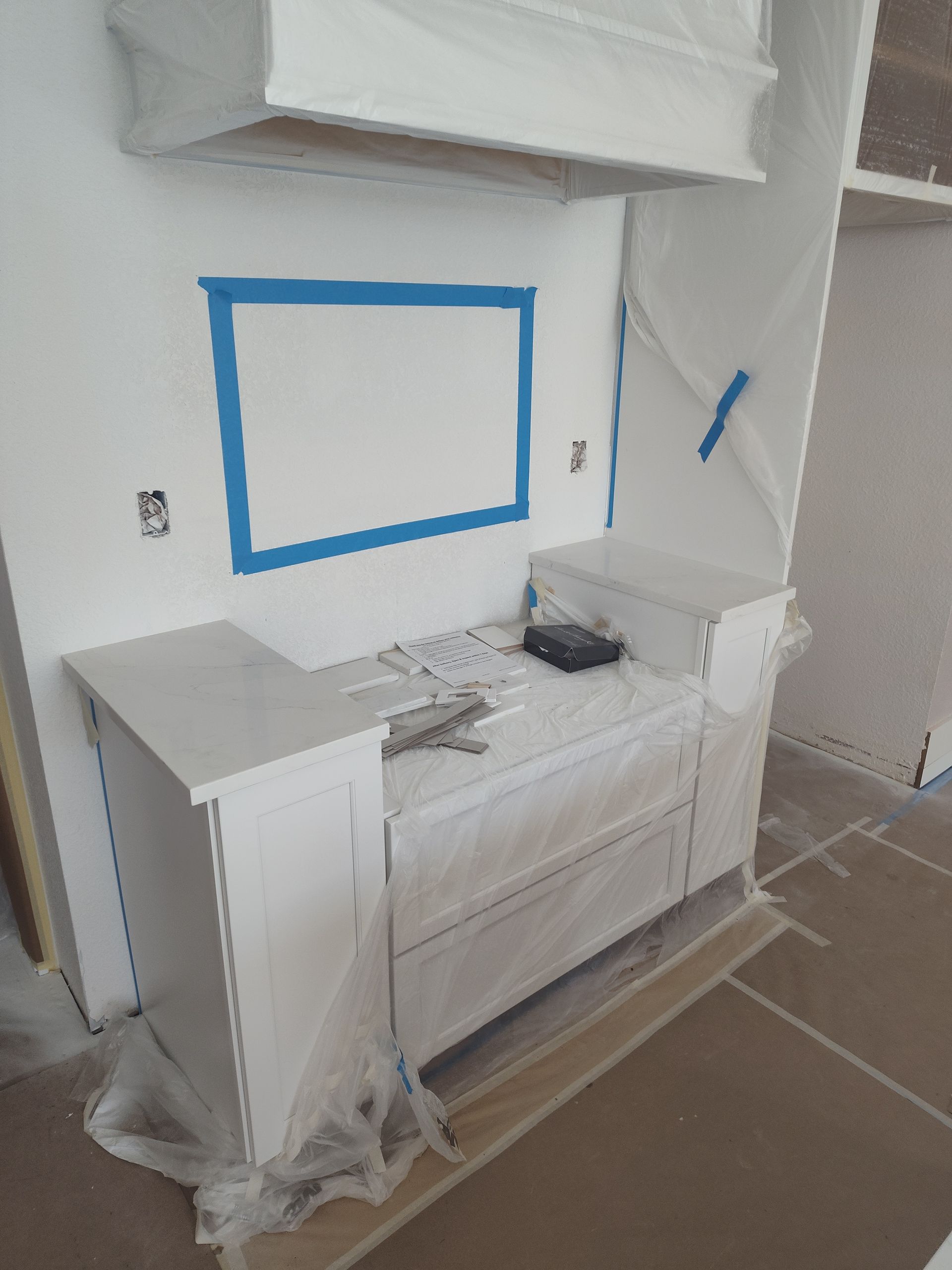 Kitchen cabinet and range hood, covered in plastic, blue tape around backsplash area, construction.