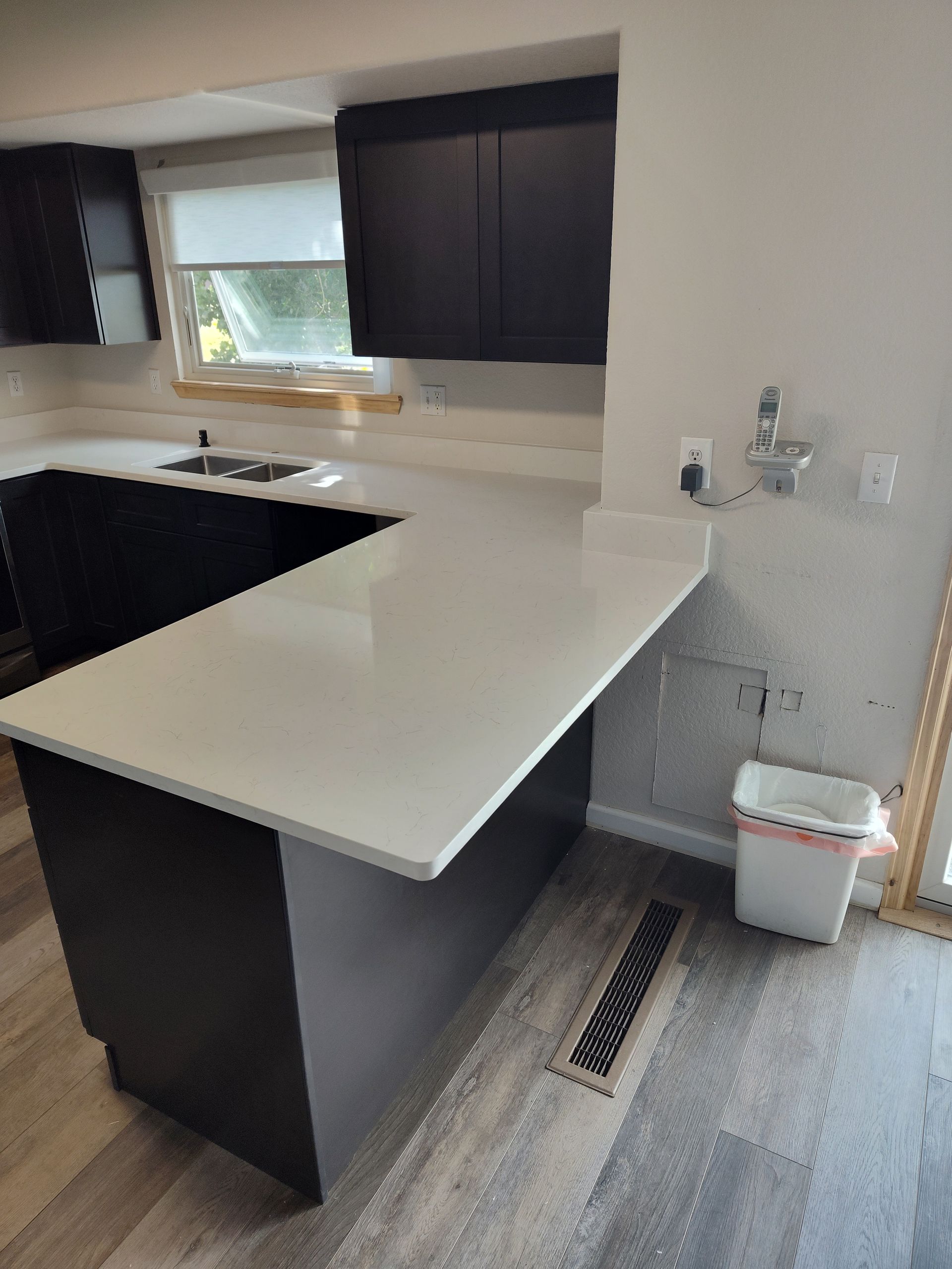 Modern kitchen with white countertop, dark cabinets, and grey flooring.
