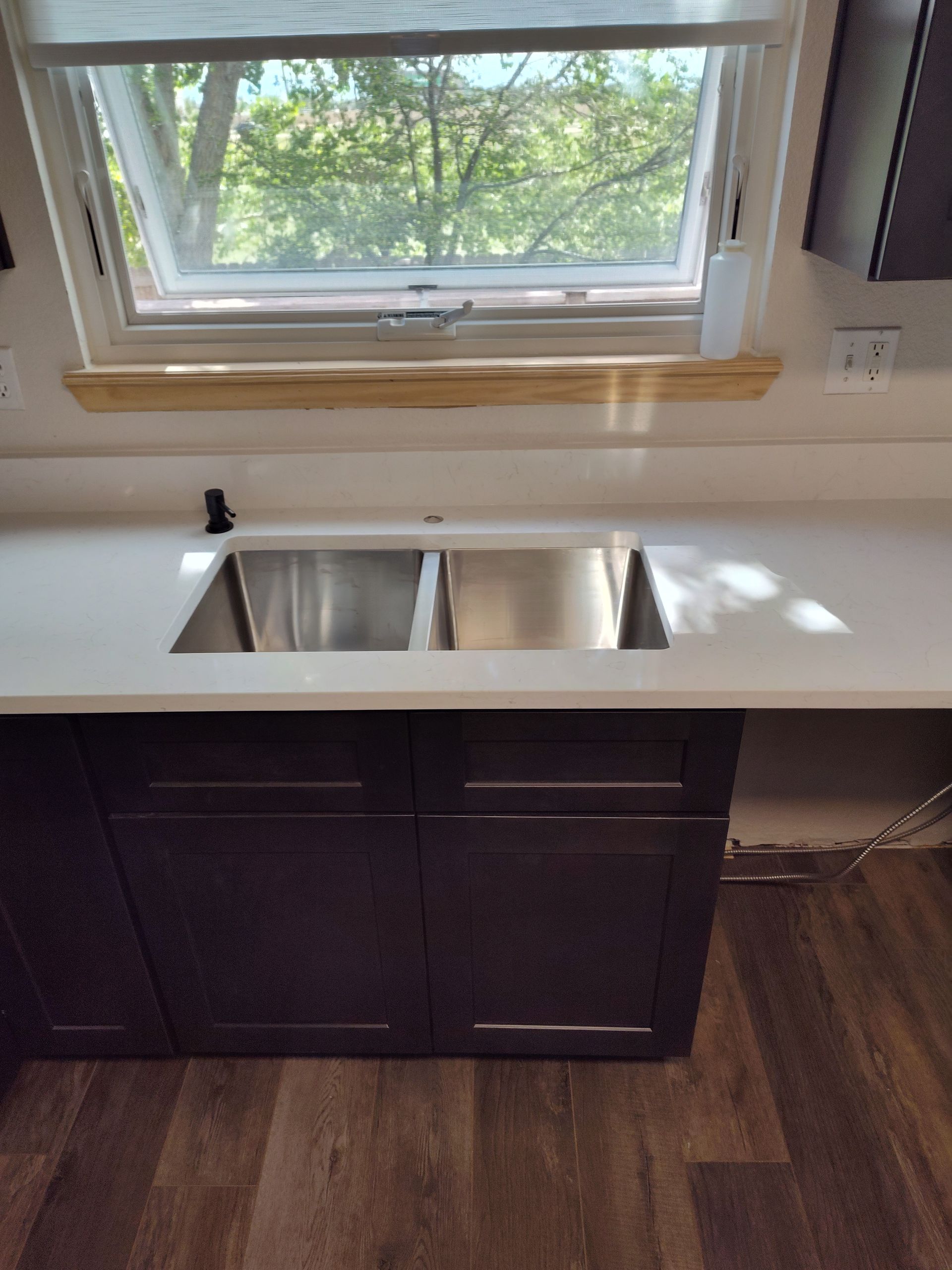 Kitchen sink with dark cabinets, white countertop, and a window above.