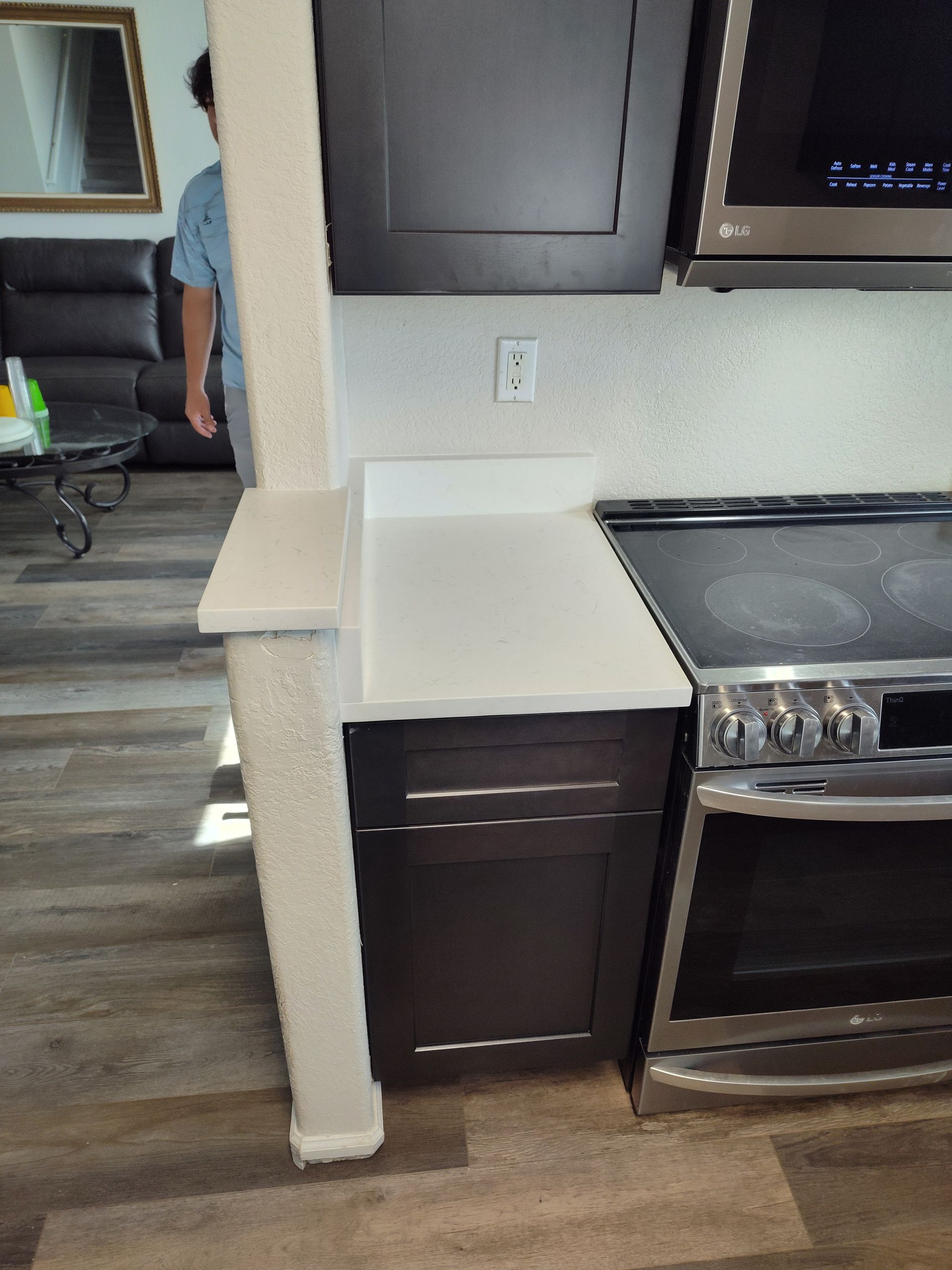 Kitchen with dark cabinets, white countertop, stainless steel stove, and a person standing in the background.