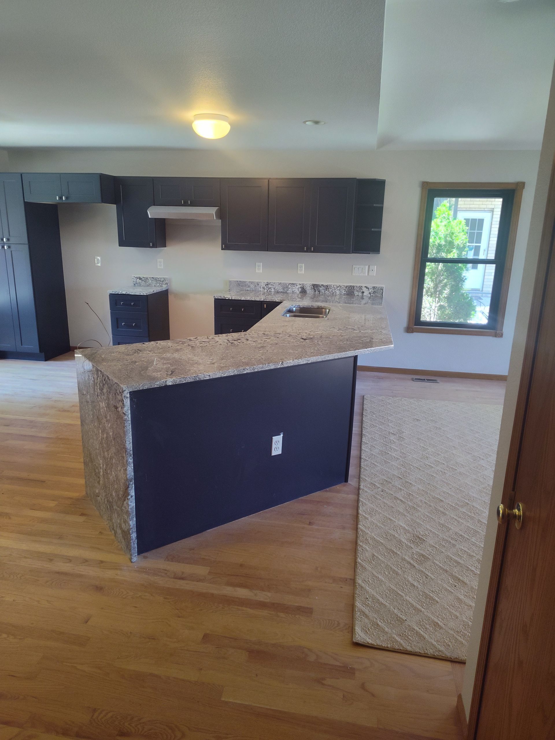 Newly renovated kitchen with a dark island and cabinets, granite countertops, and hardwood floors.