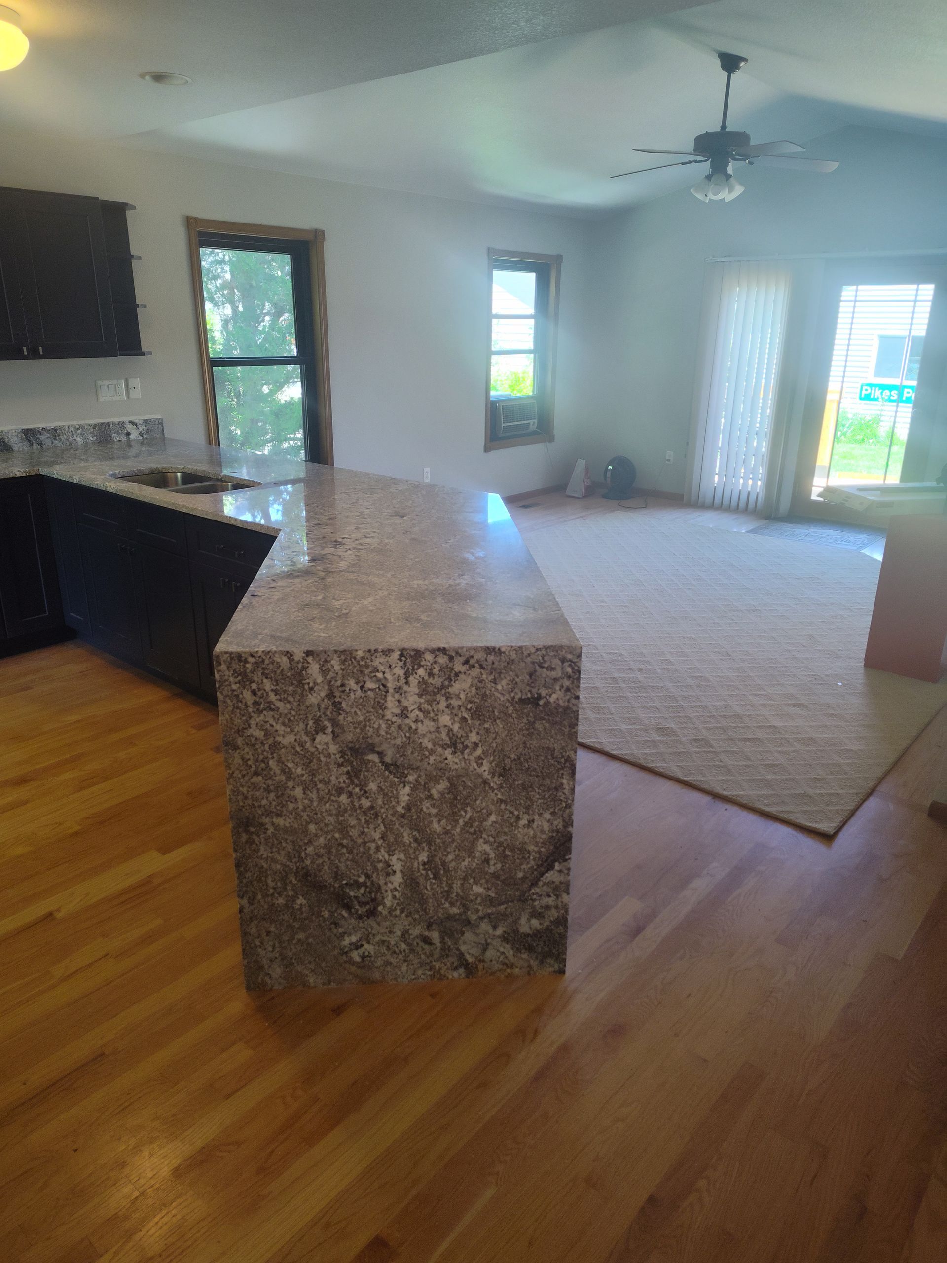 Kitchen with granite island, hardwood floors, and a living room in the background.