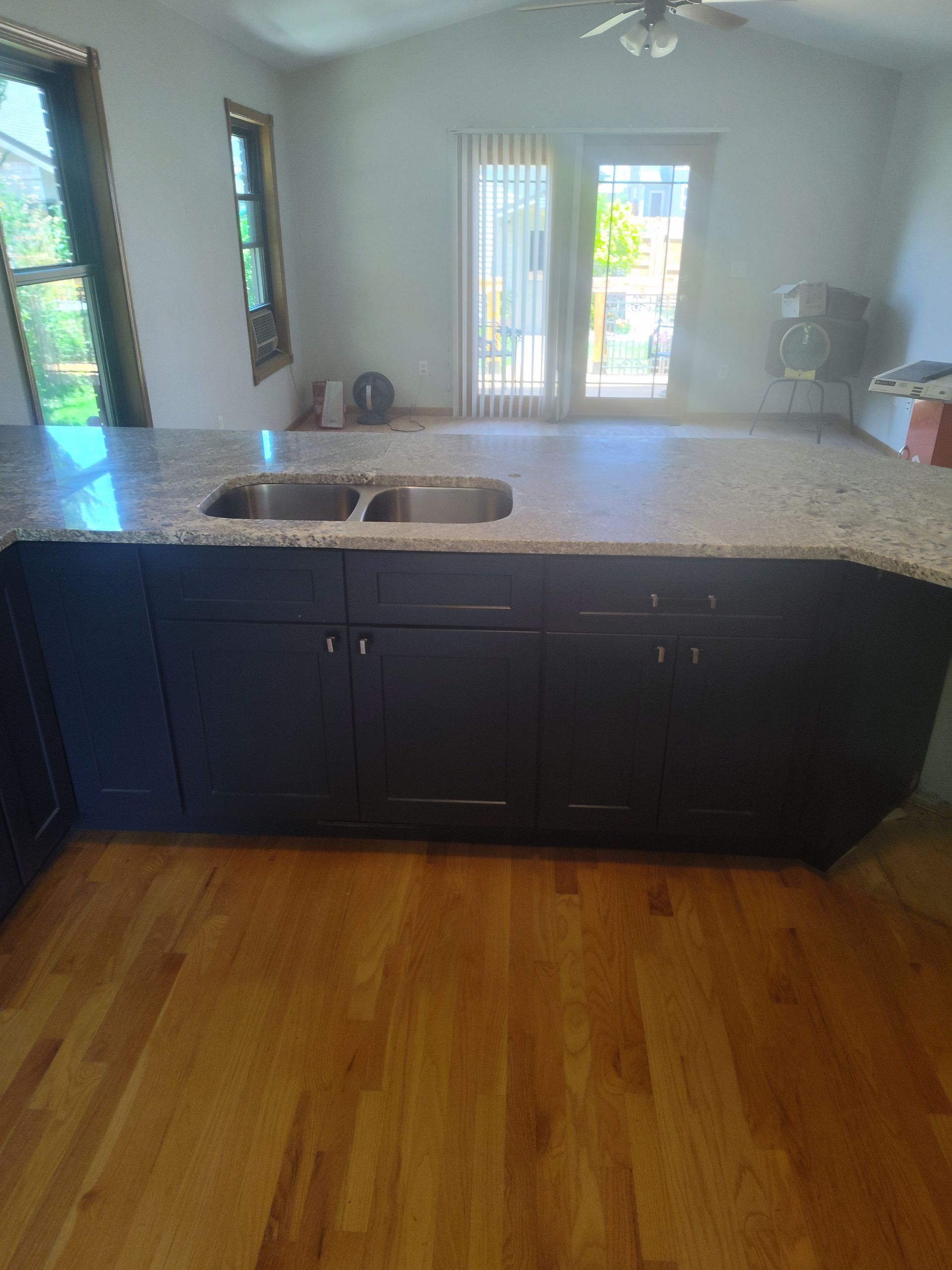 Dark blue kitchen island with granite countertop, sink, and cabinets on hardwood floor.