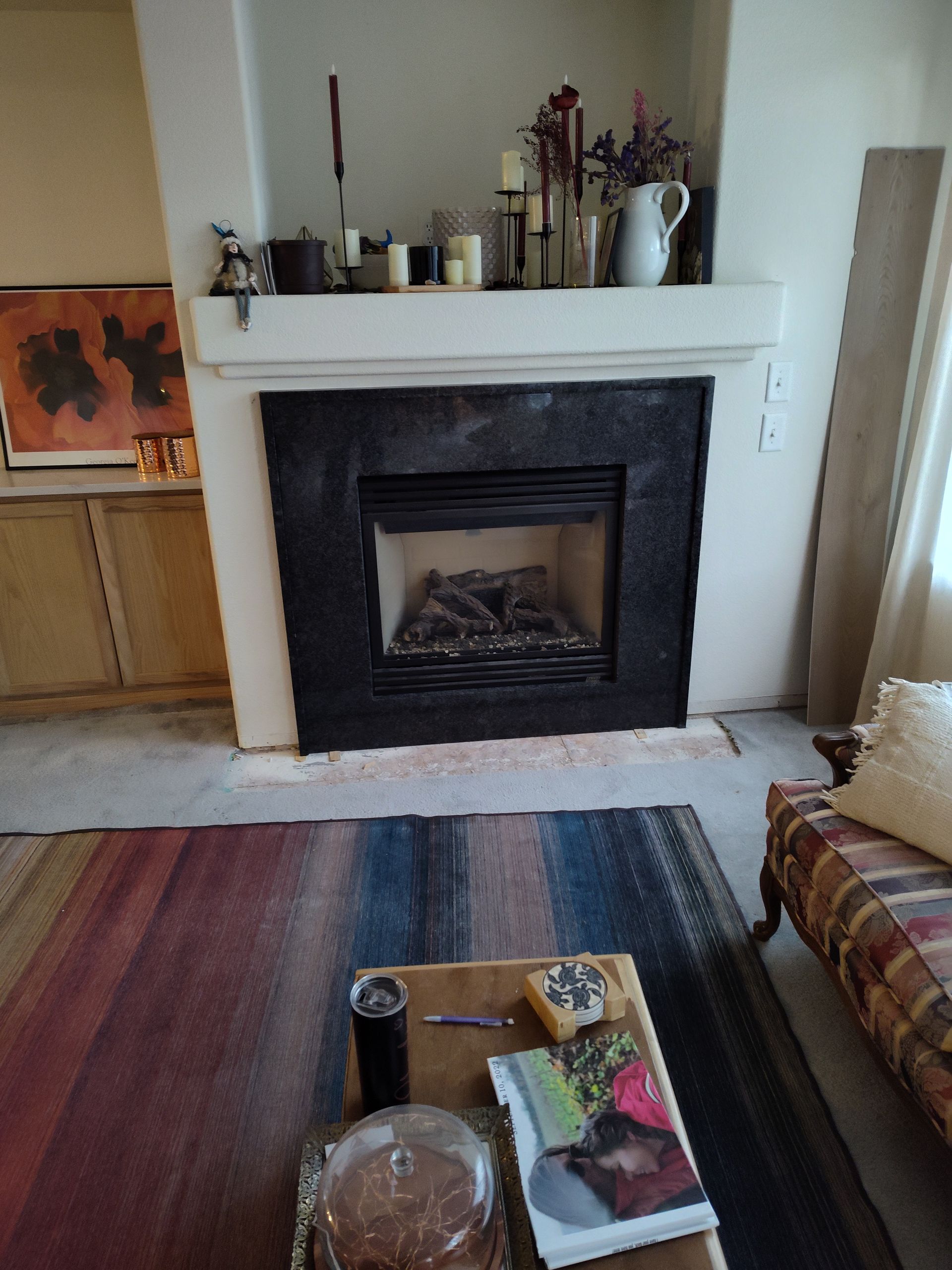 Fireplace with black surround and mantel, decorated with candles and flowers. A rug and coffee table are in front.