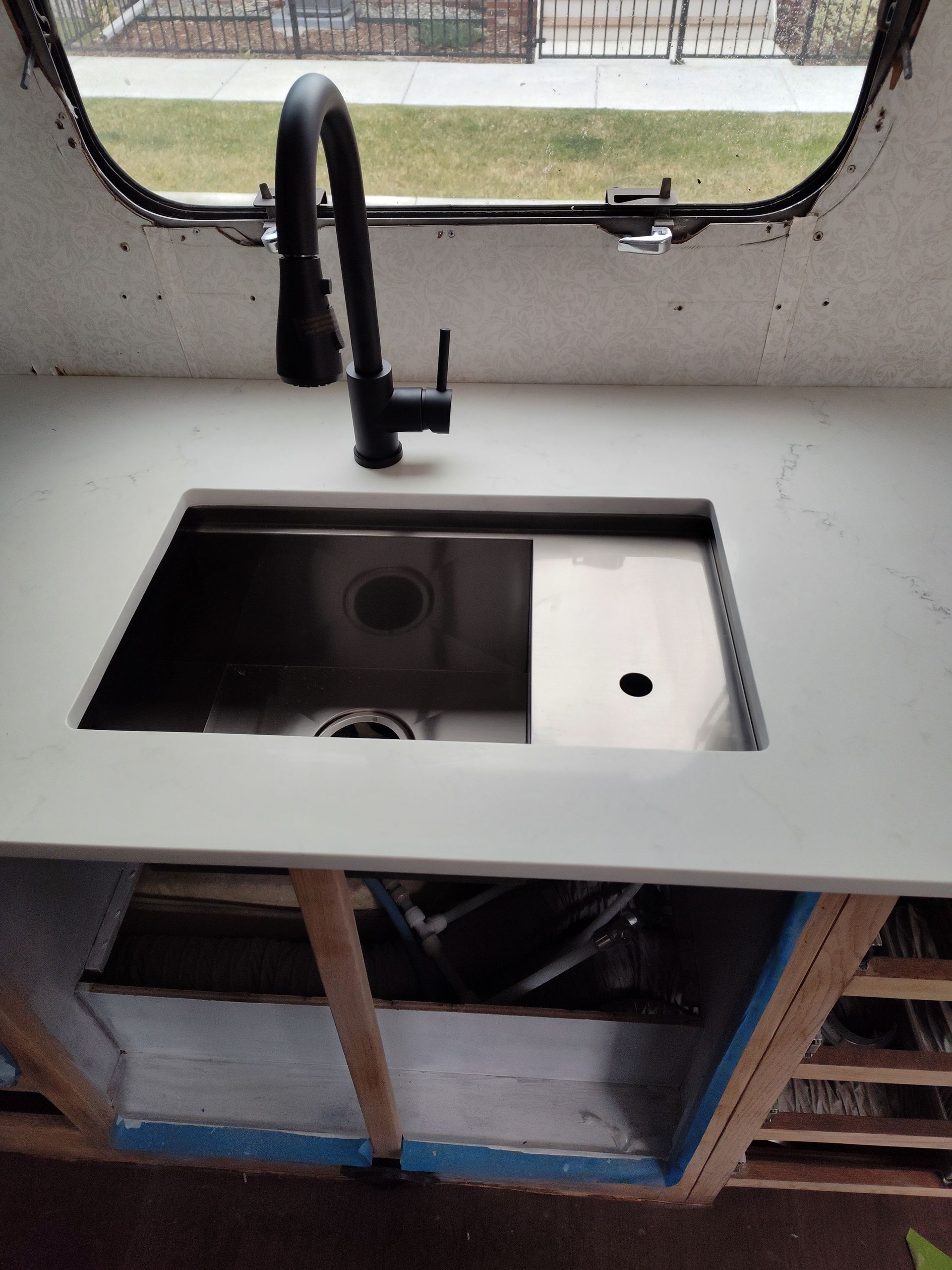 Black faucet over a stainless steel sink in a white countertop. Cabinet in progress.