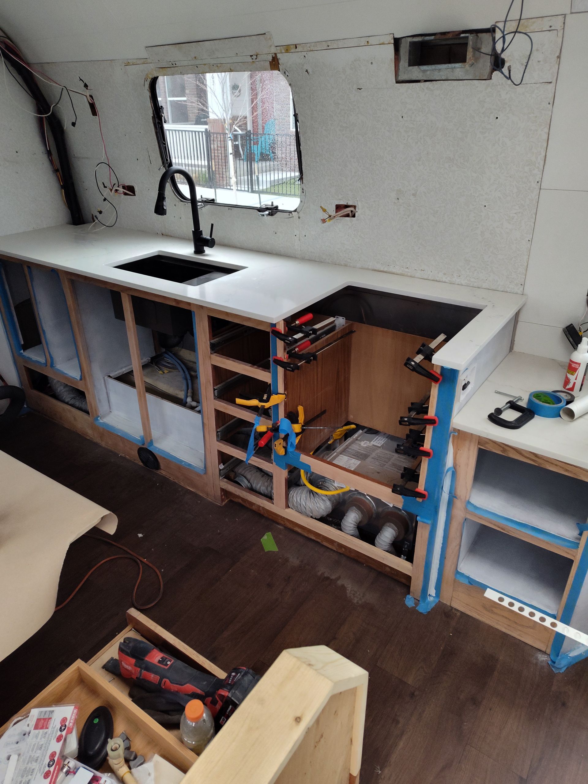 Interior of a remodeled RV kitchen with a new sink, countertop, cabinets, and window.