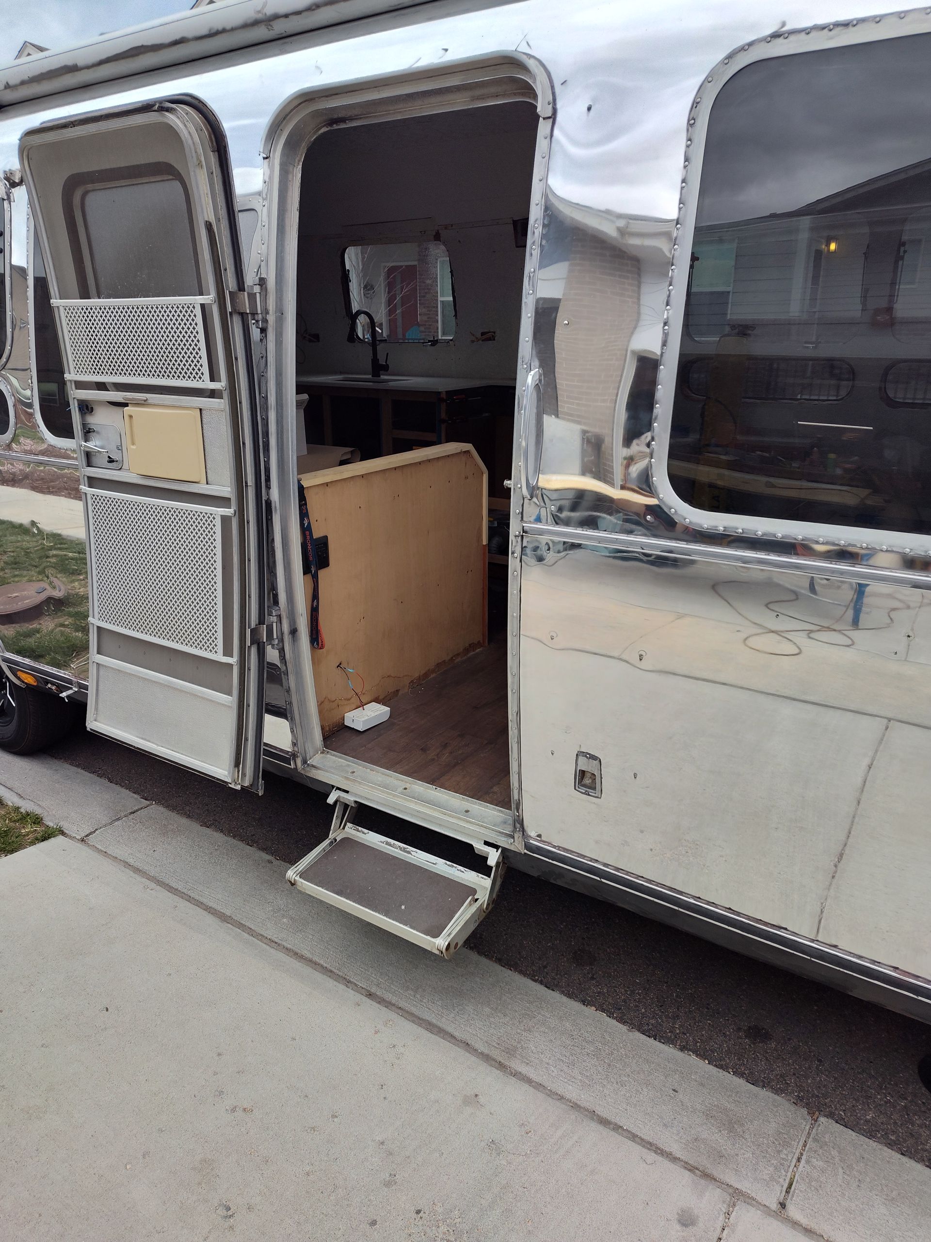 Silver Airstream trailer with open door and step. Interior visible, parked on a paved street.