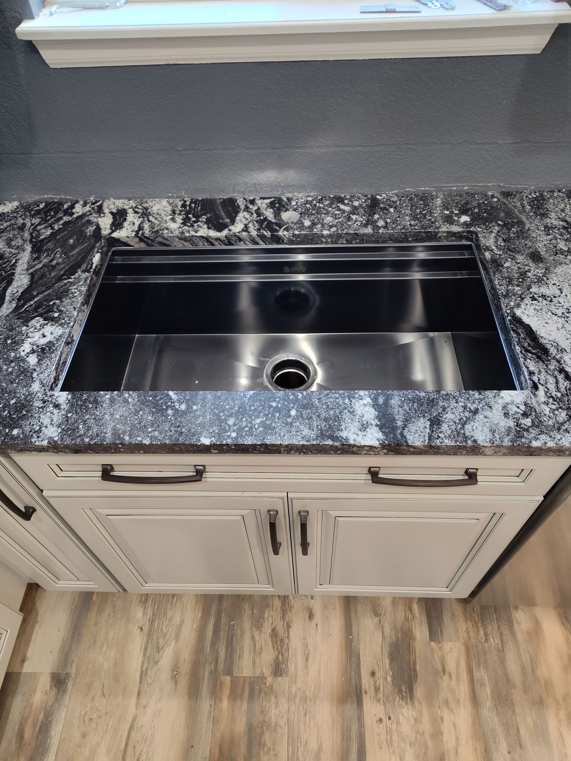 Stainless steel kitchen sink in a black and white speckled countertop, over white cabinets.