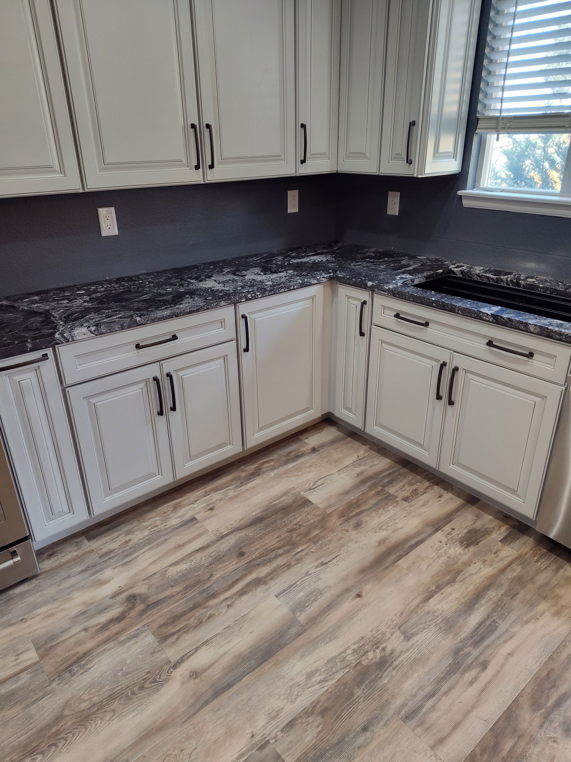 White kitchen cabinets with black countertops and wood-look floors.