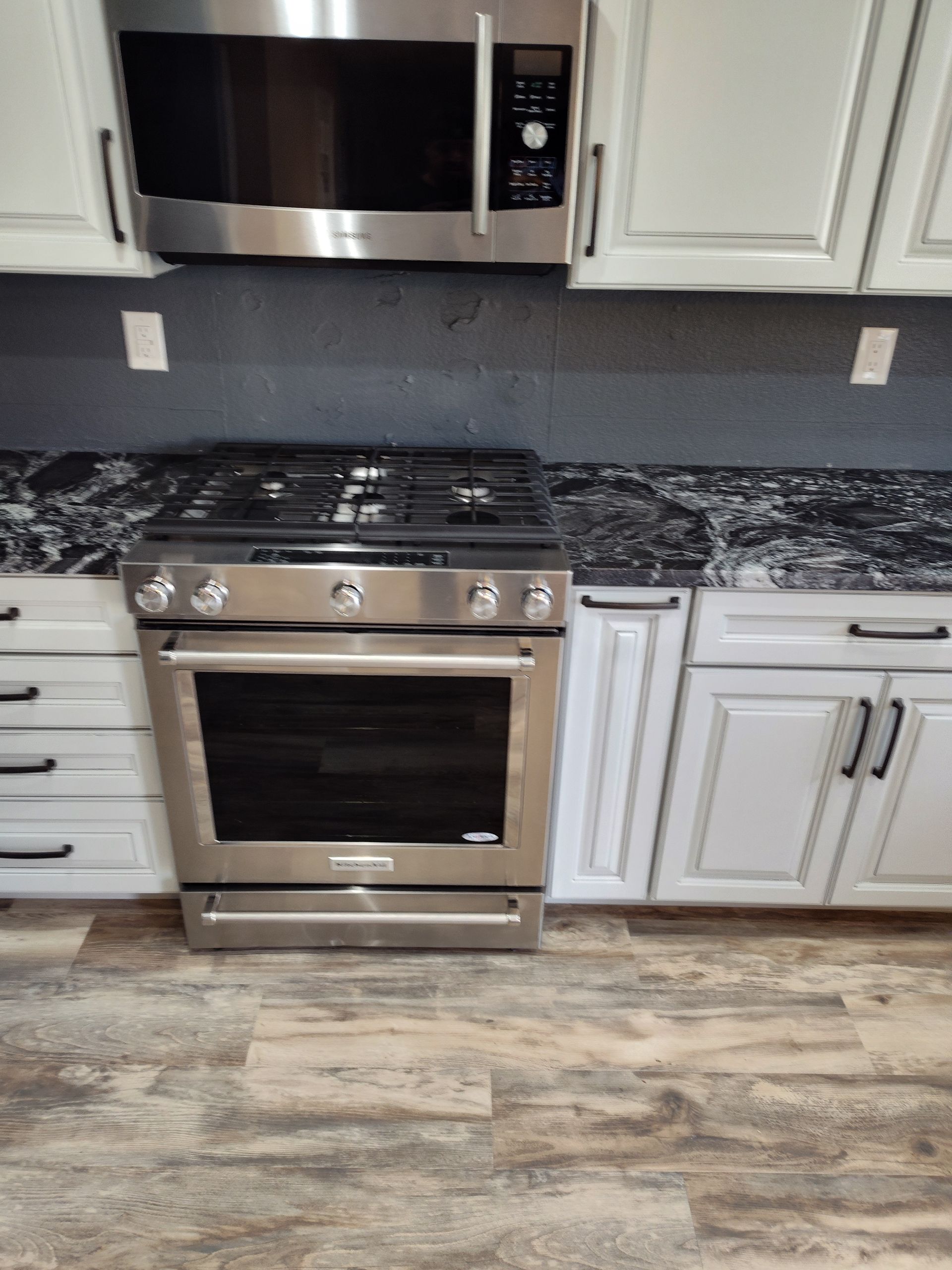 Stainless steel stove in a kitchen with white cabinets and dark countertops.