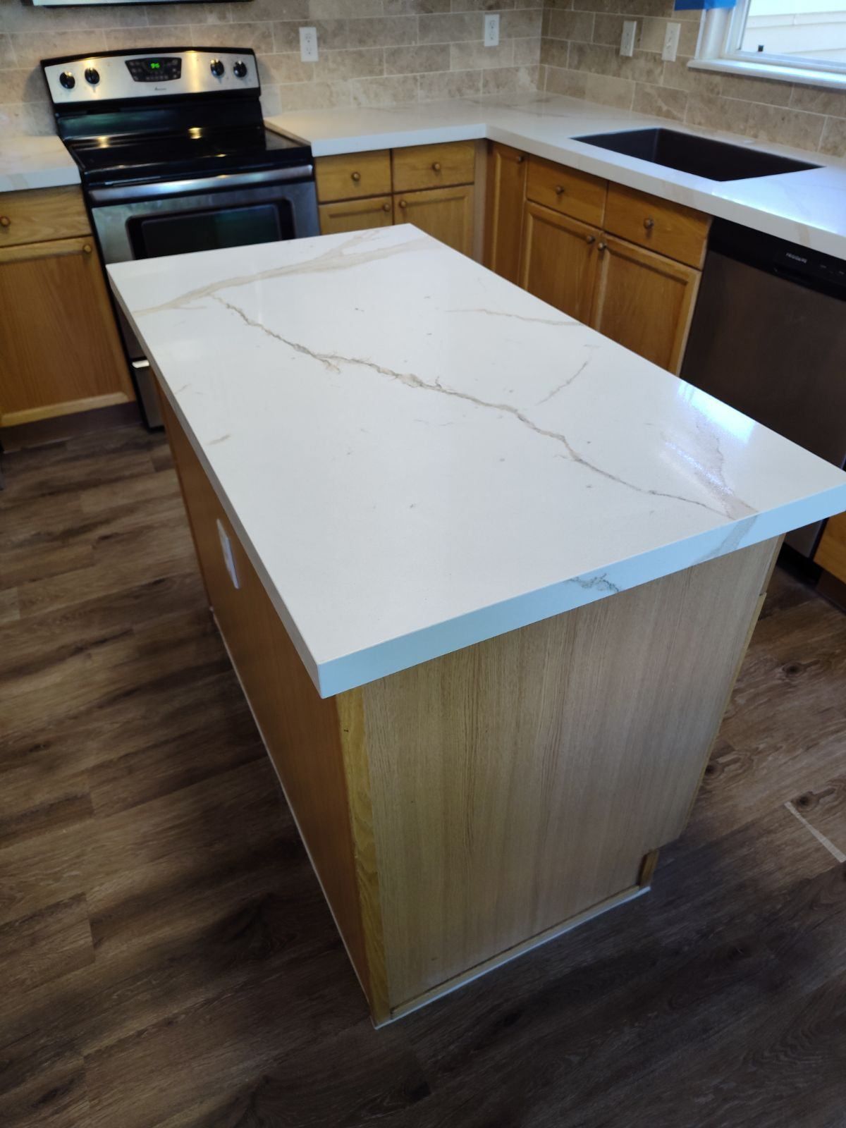 Kitchen island with white countertop, light wood cabinets, and a stainless steel stove.