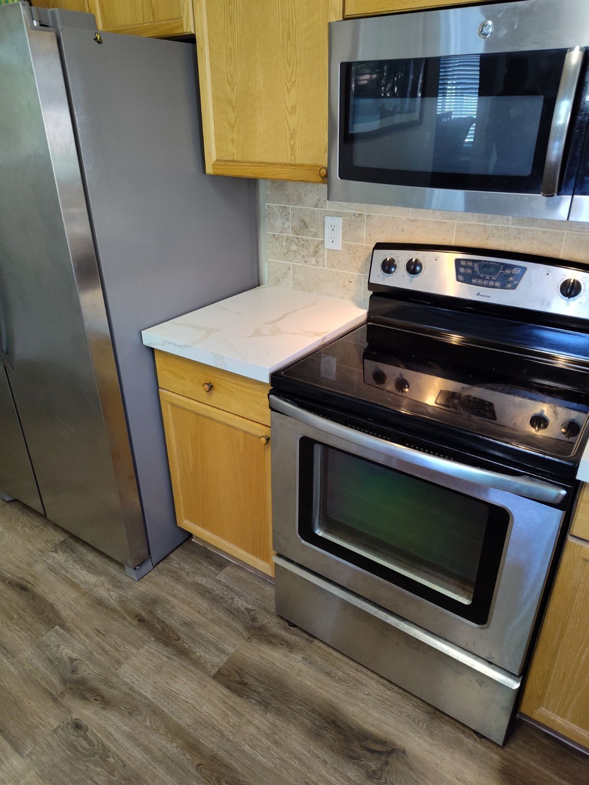 Kitchen with stainless steel appliances, light cabinets, white countertop, and backsplash.
