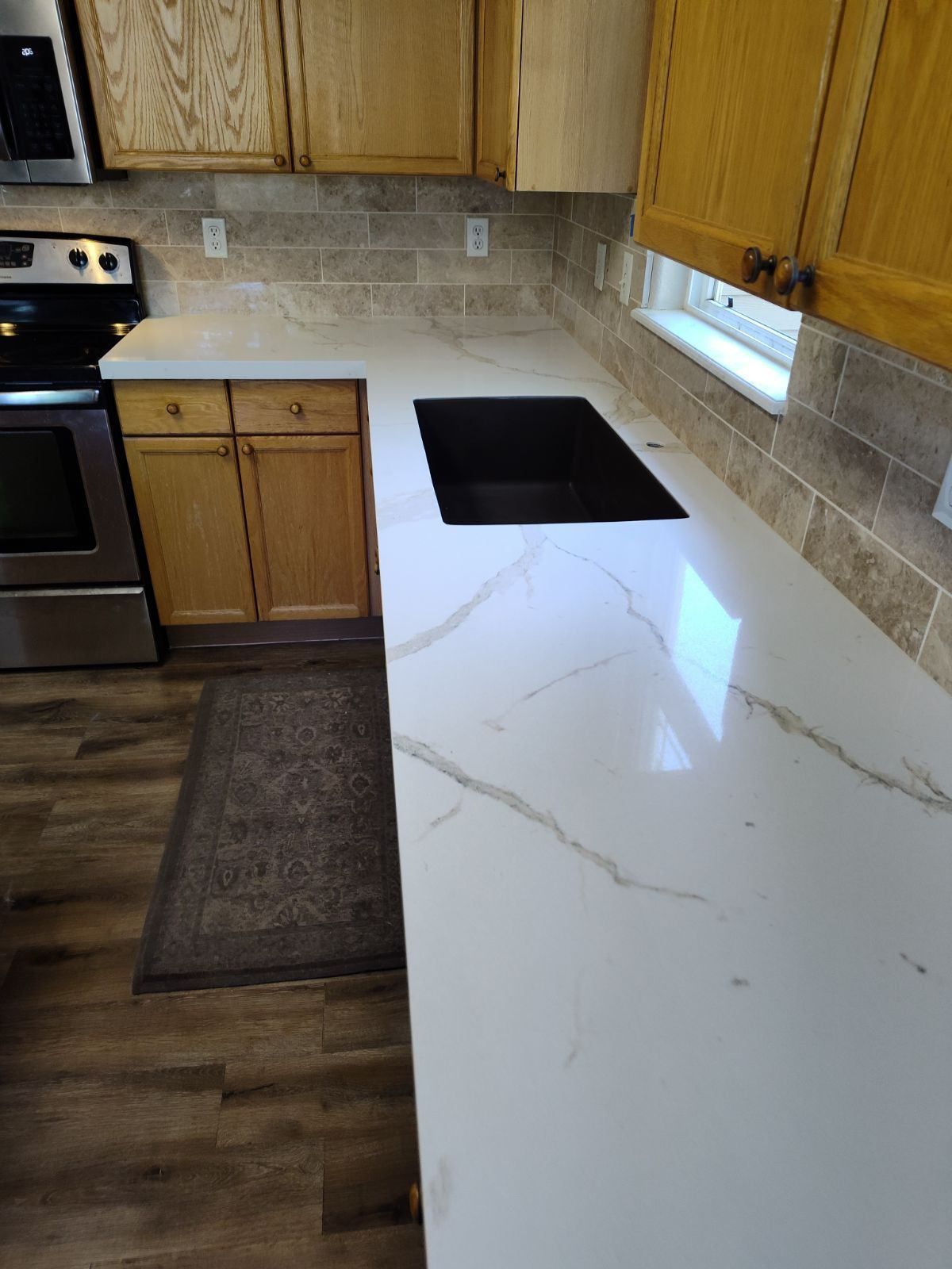 Kitchen with light countertops, wood cabinets, cooktop, and wood-look flooring.