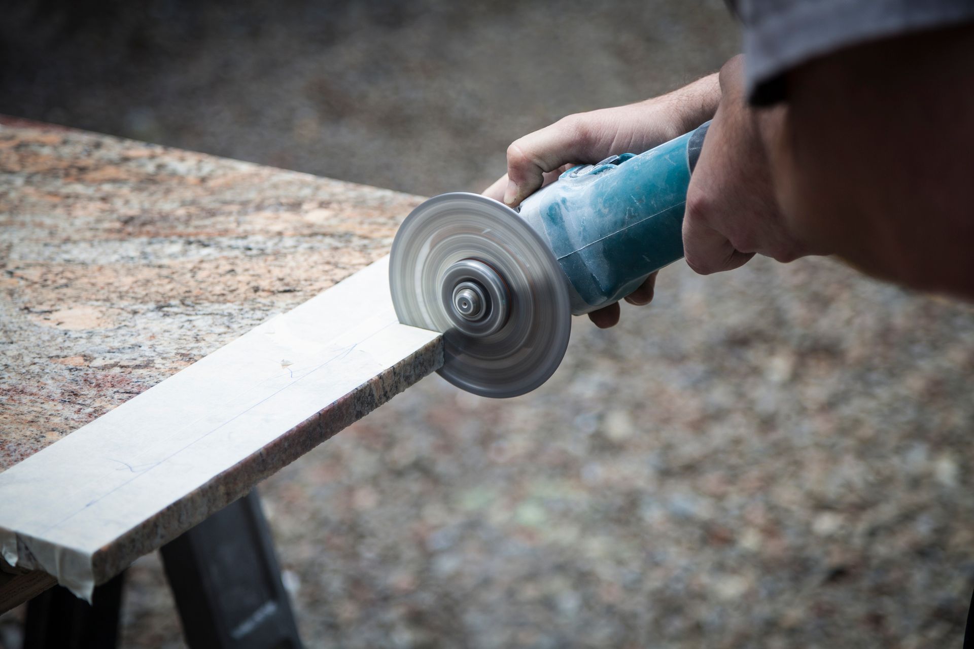 A person using a power grinder to cut a white plank on a workbench outdoors.