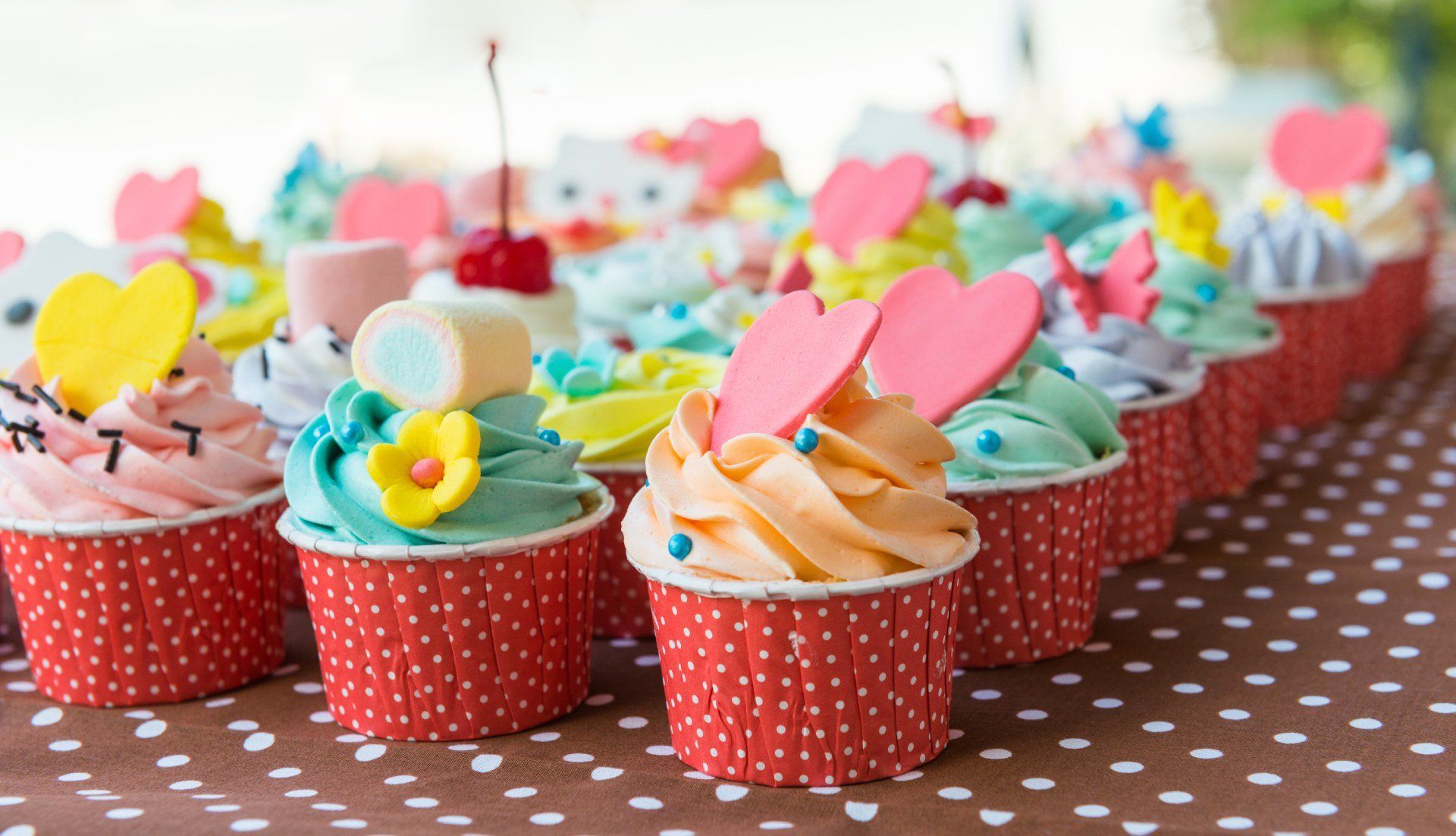 Una vetrina di cupcake decorati con glassa colorata, decorazioni a forma di cuore e zuccherini colorati, in pirottini rossi a pois.