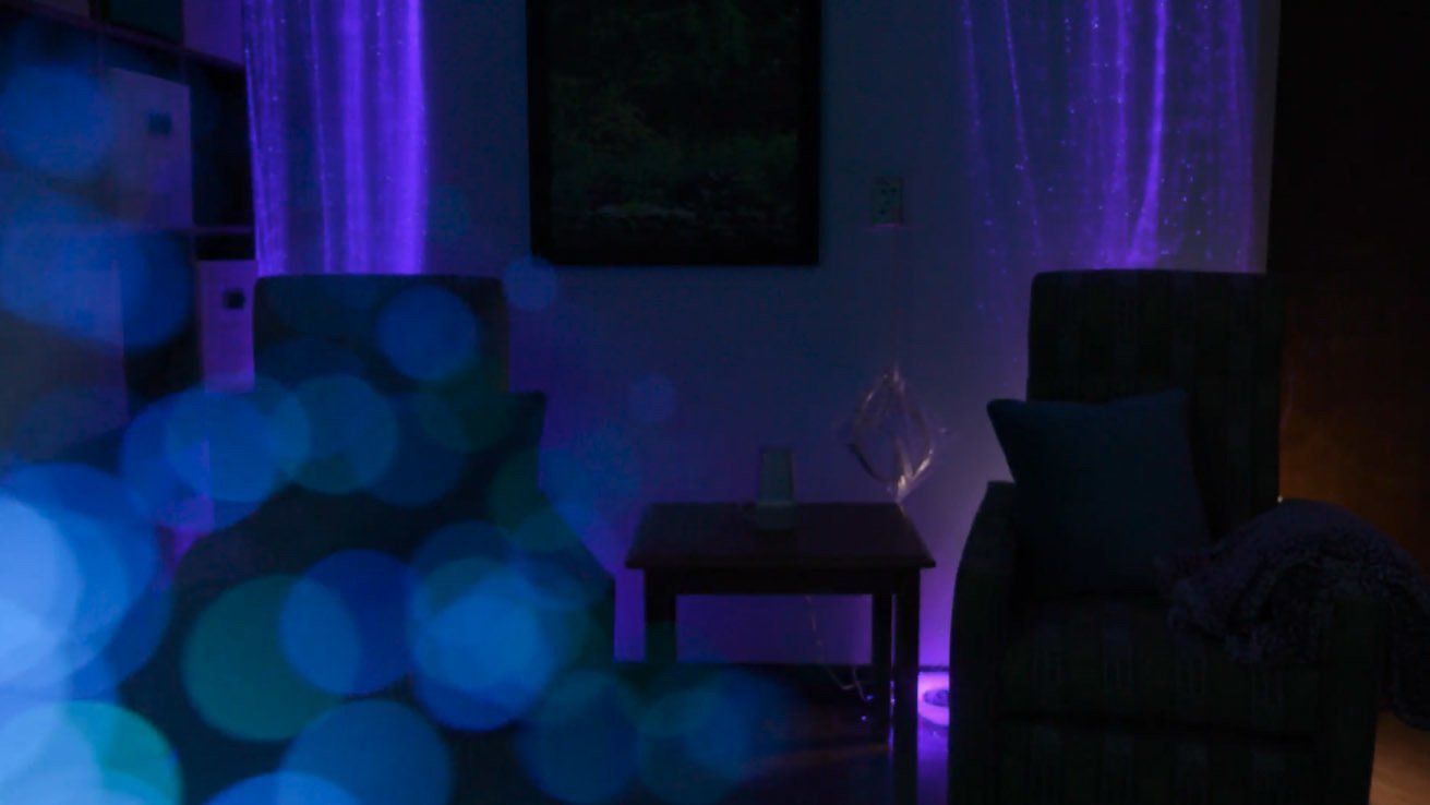 A living room with a couch , table , chair and purple lights.