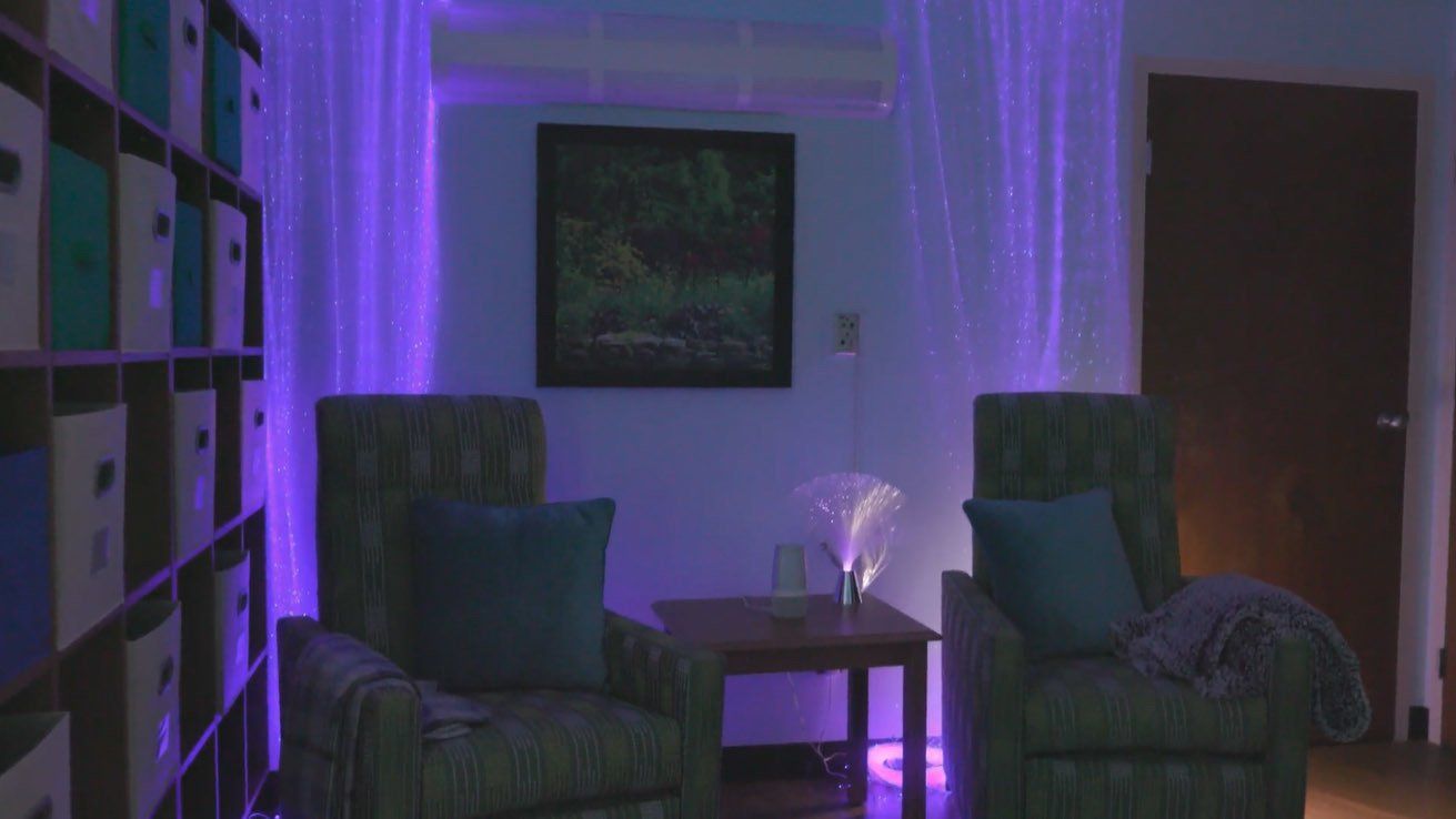 A living room with two chairs and a table with purple lights on the wall.