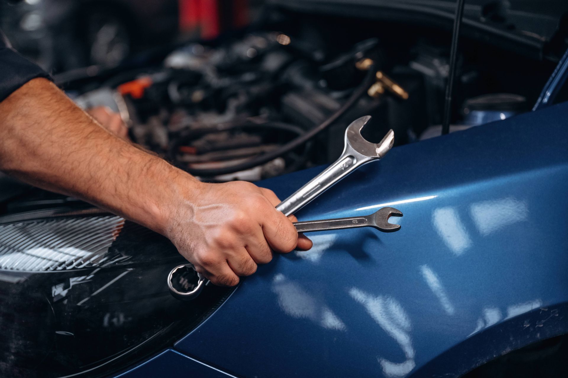 Mechanic holding two wrenches while working on an older blue car at Mr. Transmission near Sharonvill