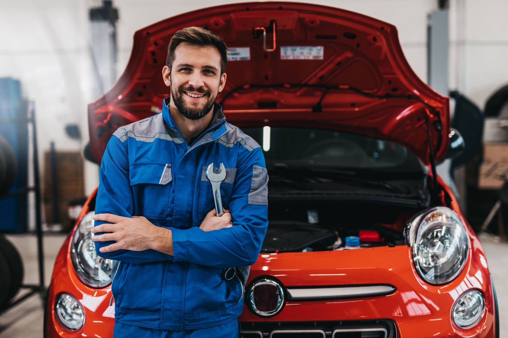 Happy car mechanic holding a wrench in front of an orange car near Cincinnati, OH