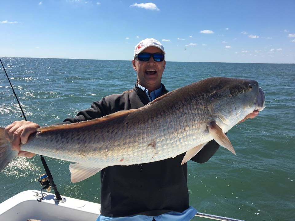 Man holding large redfish on a boat, smiling, with ocean in the background.