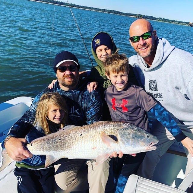 Family on a boat, holding a large fish.  Water and sky are visible. Happy expressions.