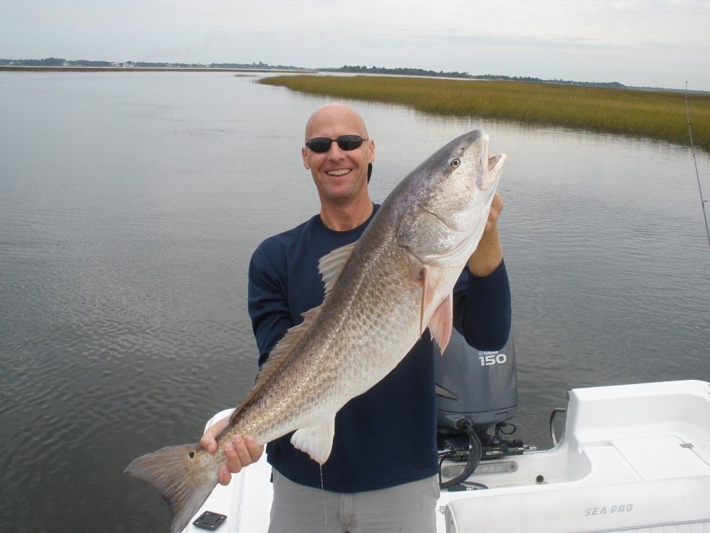 Man on boat holding large redfish. Outdoors, cloudy sky.