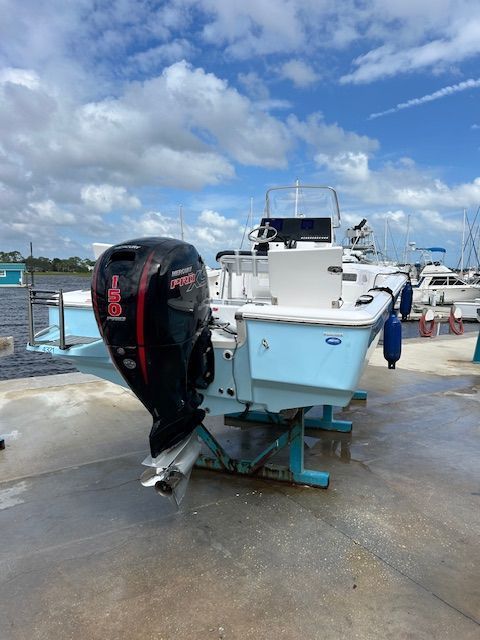 A light blue and white fishing boat with a black motor sits on a dock under a cloudy blue sky.