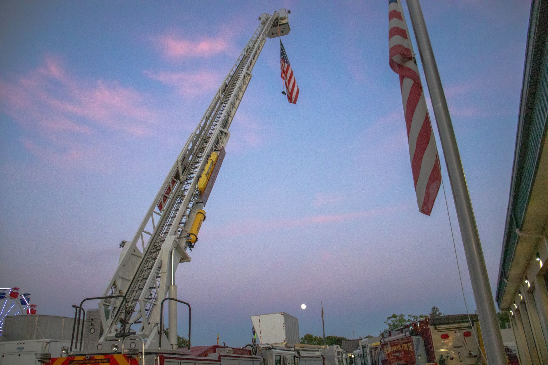 A firetruck ladder is lifting an American flag in the air
