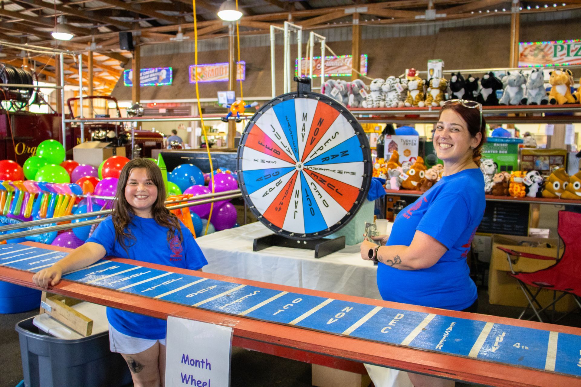 Two women are standing next to a game wheel in a carnival.