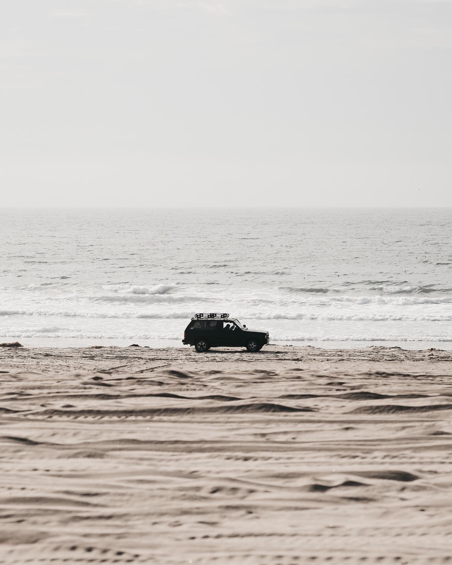 A Car Is Driving On A Sandy Beach Near The Ocean — Torque Tyres & Trailer Spares Mackay in Mackay, QLD