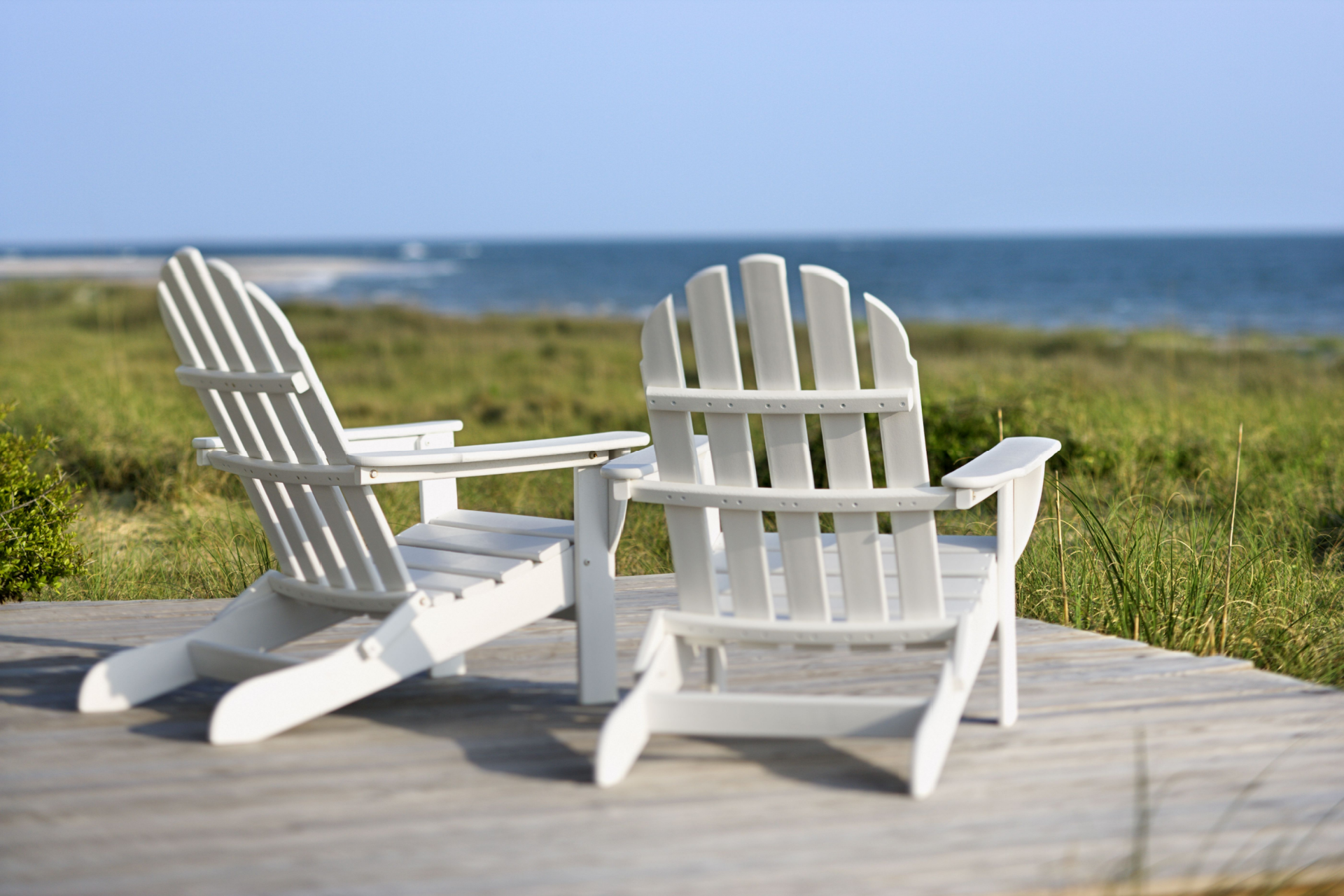 Two white adirondack chairs are sitting on a wooden deck overlooking the ocean.