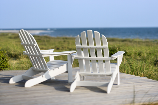 Two white adirondack chairs are sitting on a wooden deck overlooking the ocean.