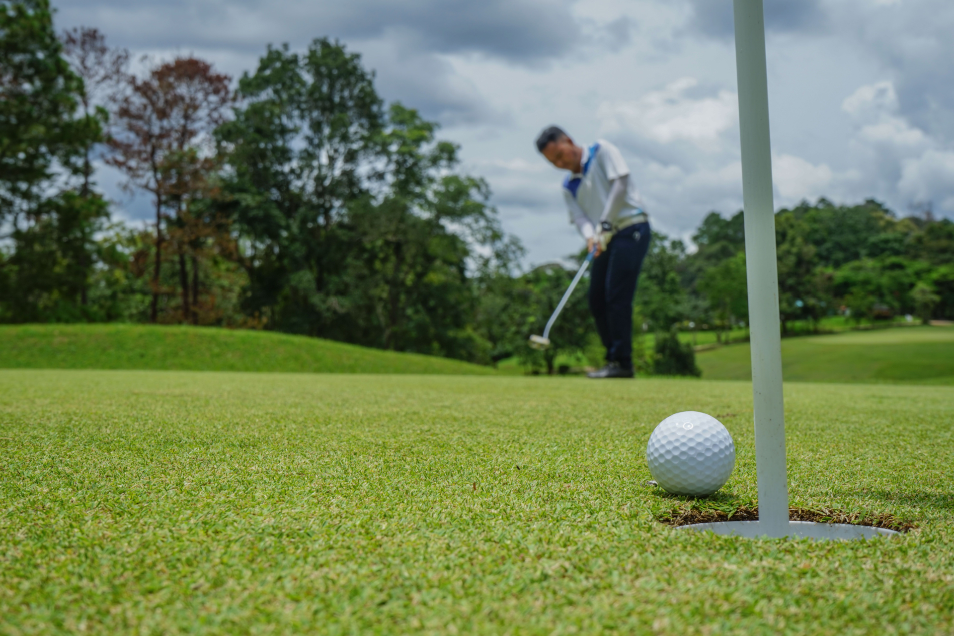 A man is swinging a golf club at a golf ball on a golf course.